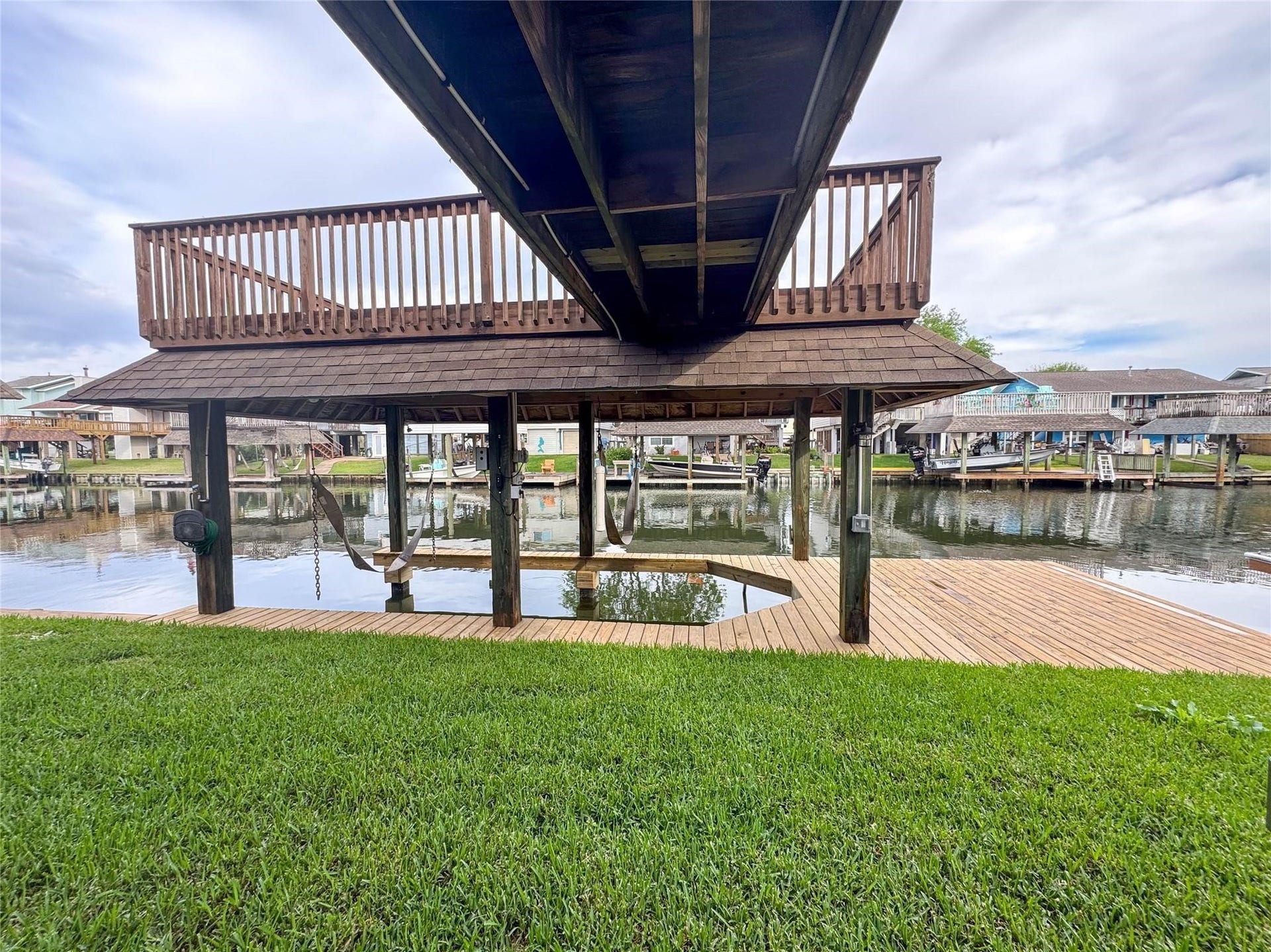 1031 Redfish Street, Bayou Vista, TX 77563 This photo showcases a waterfront property featuring a wooden dock with a covered boat lift and an upper deck. The area offers direct access to the water, perfect for boating enthusiasts. The surrounding neighborhood is visible across the canal, providing a serene, picturesque view.