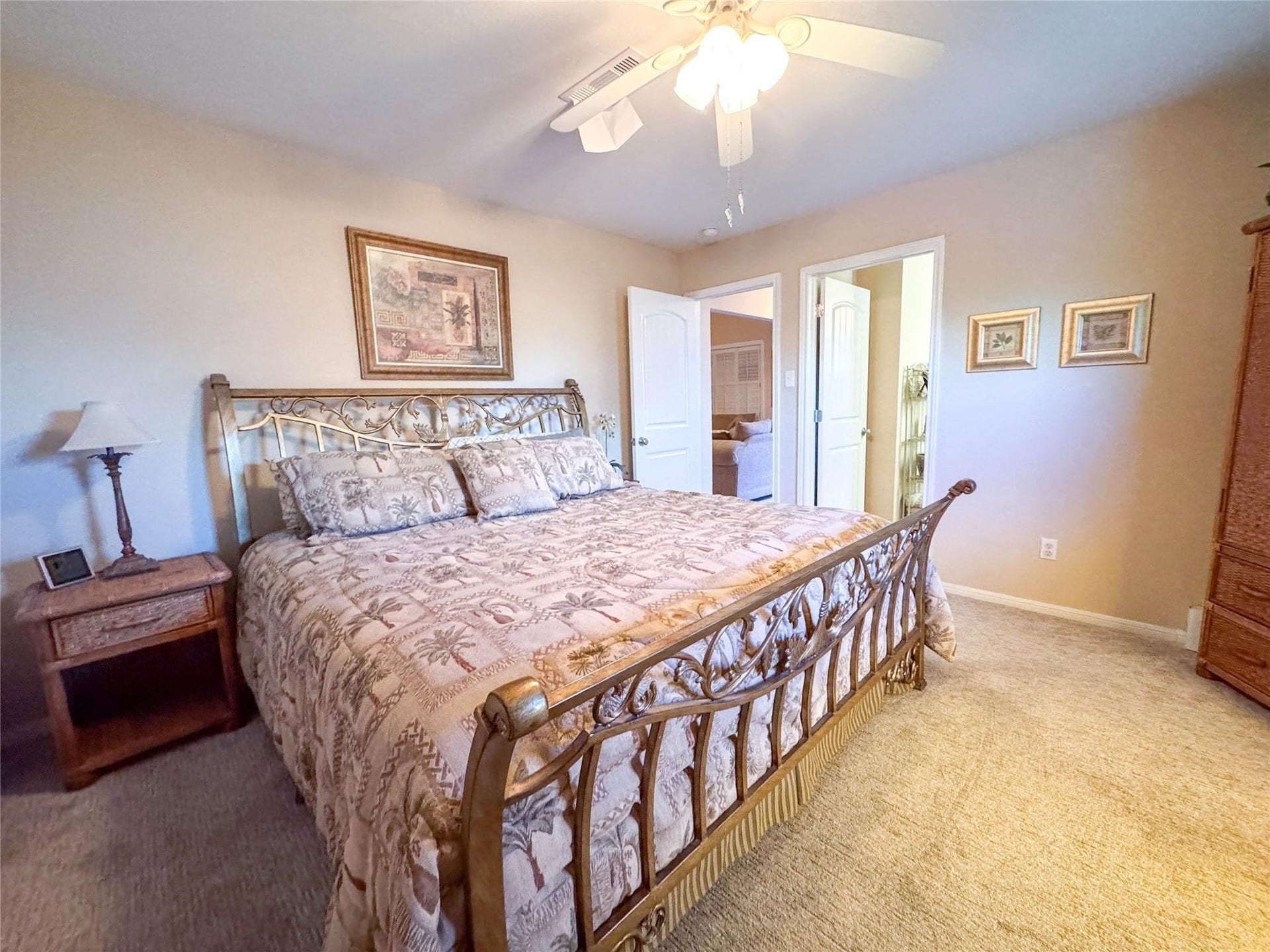 1031 Redfish Street, Bayou Vista, TX 77563 Cozy bedroom featuring a stylish metal bed frame, soft carpeting, and warm neutral walls. It includes a ceiling fan, wooden nightstand with a lamp, and tasteful wall art, creating a welcoming atmosphere.