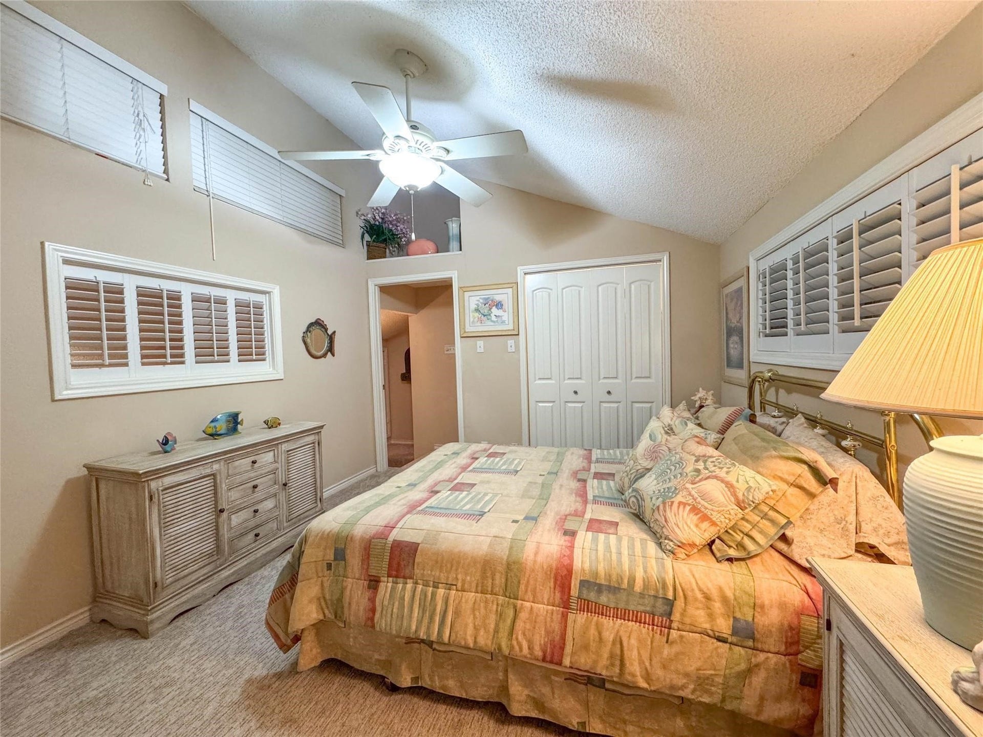 1031 Redfish Street, Bayou Vista, TX 77563 Cozy bedroom with vaulted ceilings, featuring a ceiling fan and soft carpeting. It includes a large bed with patterned bedding, ample closet space, and natural light from multiple windows with shutters, creating a warm and inviting atmosphere.