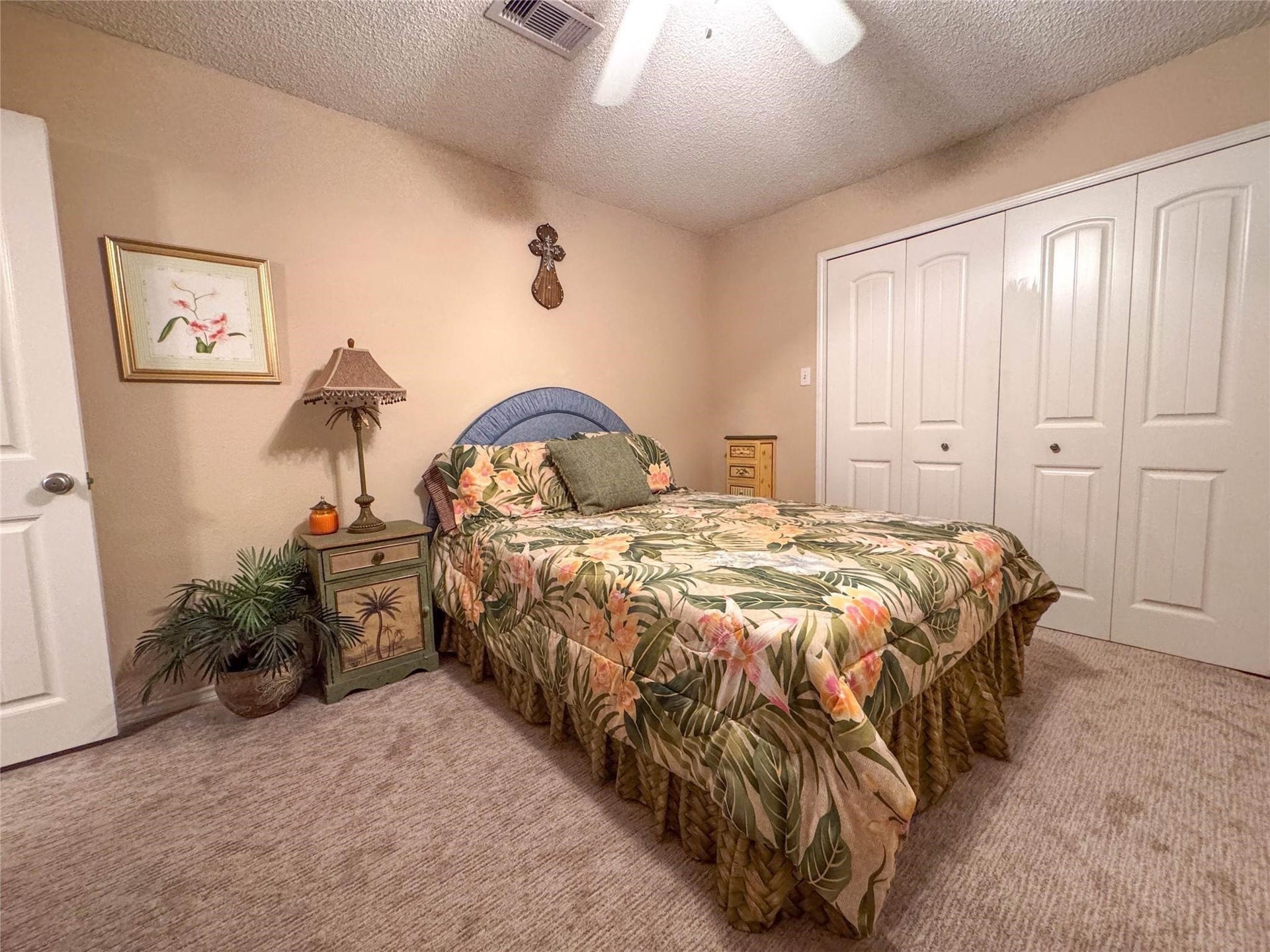 1031 Redfish Street, Bayou Vista, TX 77563 Cozy bedroom with a tropical theme, featuring a floral bedspread, a ceiling fan, and ample closet space. Warm beige walls and carpet create a welcoming atmosphere.