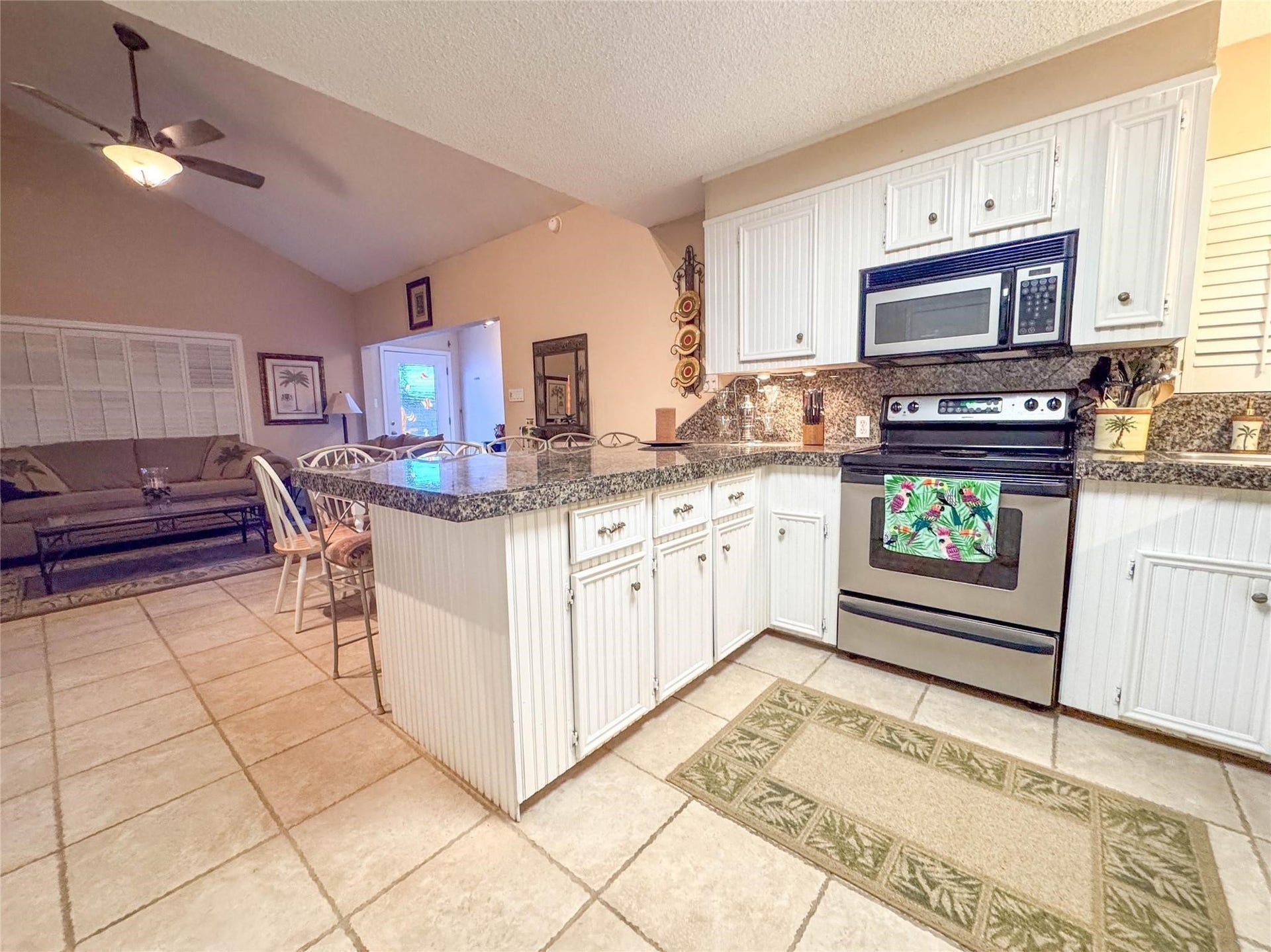 1031 Redfish Street, Bayou Vista, TX 77563 This inviting open-concept space features a cozy living area adjacent to a modern kitchen with granite countertops, white cabinetry, and stainless steel appliances. The tile flooring and vaulted ceiling enhance the room's spacious feel, perfect for relaxed living and entertaining.