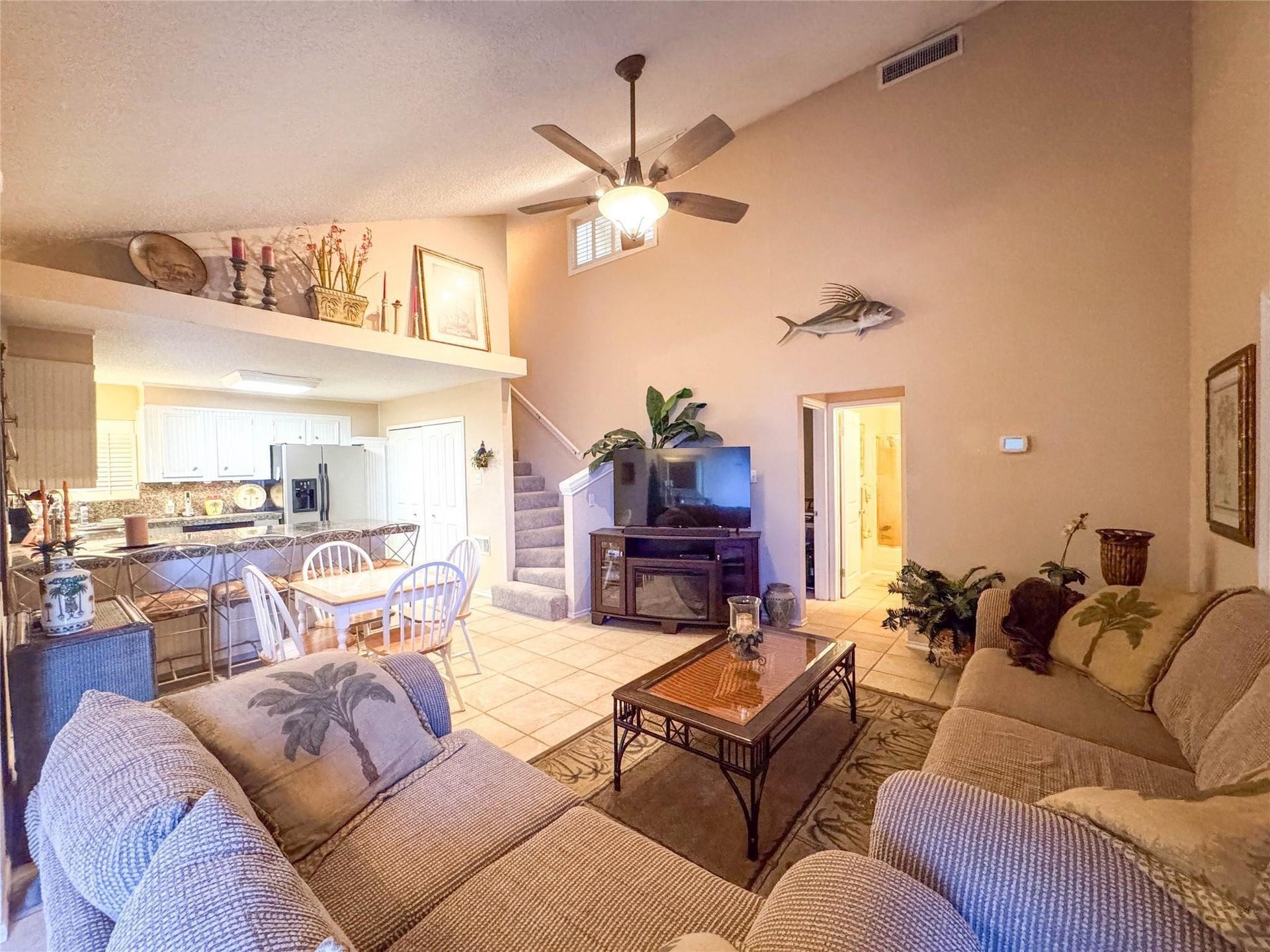 1031 Redfish Street, Bayou Vista, TX 77563 This inviting living space features high ceilings and an open layout with cozy seating, a ceiling fan, and decorative touches. The adjacent kitchen and dining area are bright and functional, with a staircase leading to the upper floor. Ideal for comfortable living and entertaining.