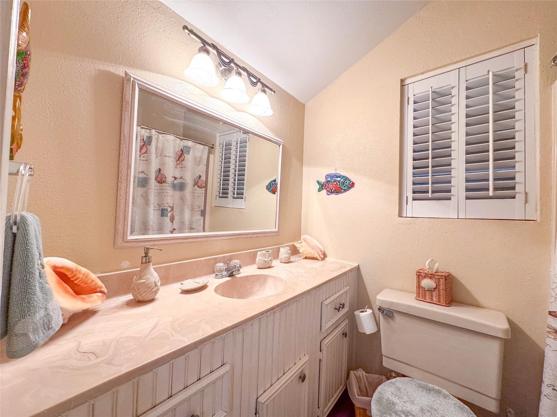 1031 Redfish Street, Bayou Vista, TX 77563 This cozy bathroom features a large vanity with ample storage, a decorative mirror, and a soft color palette. It includes a stylish light fixture, charming window shutters, and a whimsical fish decoration, creating a welcoming atmosphere.