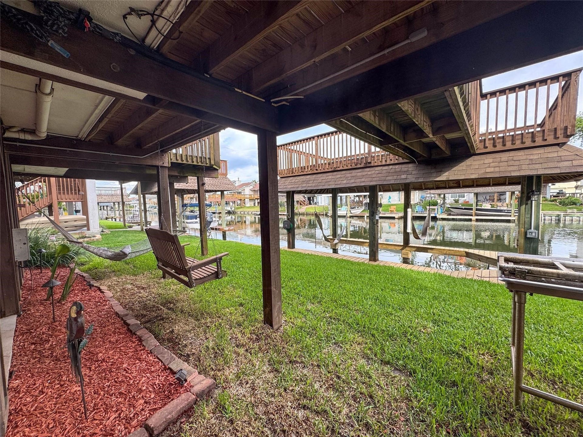 1031 Redfish Street, Bayou Vista, TX 77563 This photo showcases a serene waterfront area with a covered patio, lush grass, and a hammock. Ideal for relaxation and enjoying canal views, it offers a peaceful outdoor retreat.