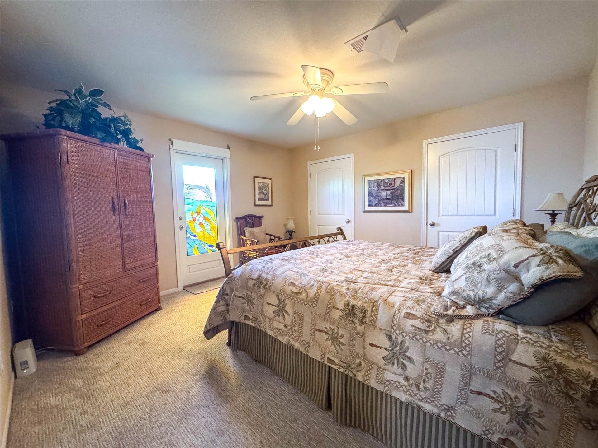 1031 Redfish Street, Bayou Vista, TX 77563 This cozy bedroom features a ceiling fan, a wicker armoire, and a bed with a tropical-themed comforter. A stained glass door adds a unique touch, complemented by neutral walls and carpet.