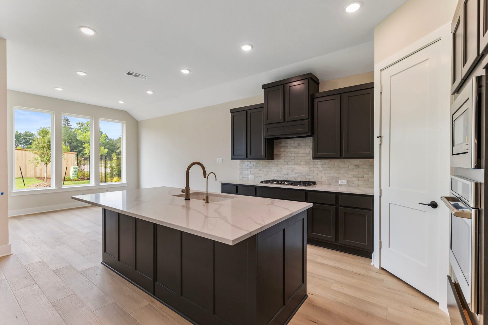 8143 Fenway Heights Dr, The Woodlands, TX 77389 Sleek modern kitchen features dark cabinetry, a spacious quartz island with a built-in sink, and stainless steel appliances.