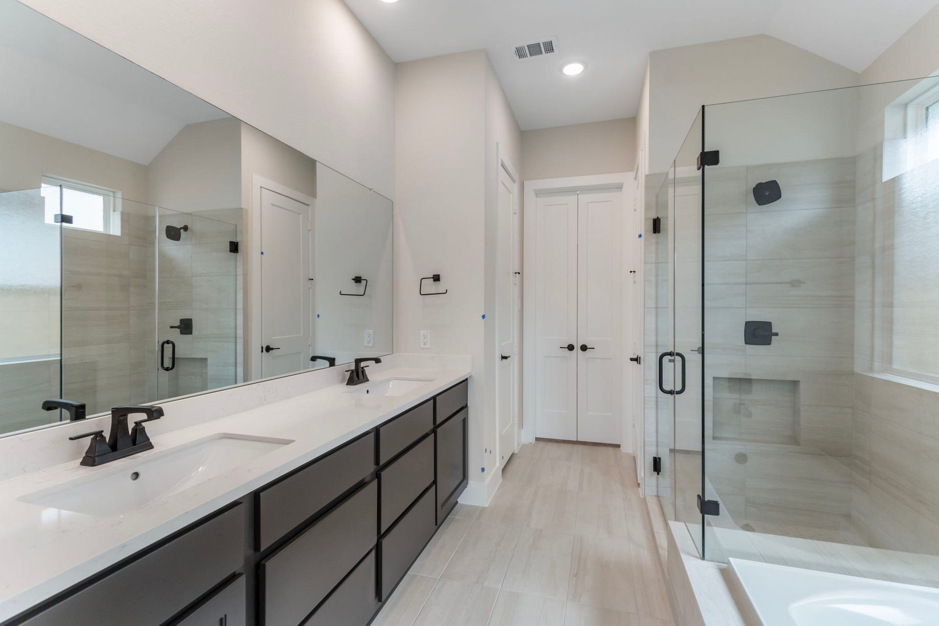 8143 Fenway Heights Dr, The Woodlands, TX 77389 Experience luxury in this modern bathroom featuring dual sinks, sleek black fixtures, a spacious glass-enclosed shower, and elegant tilework for a sophisticated touch.