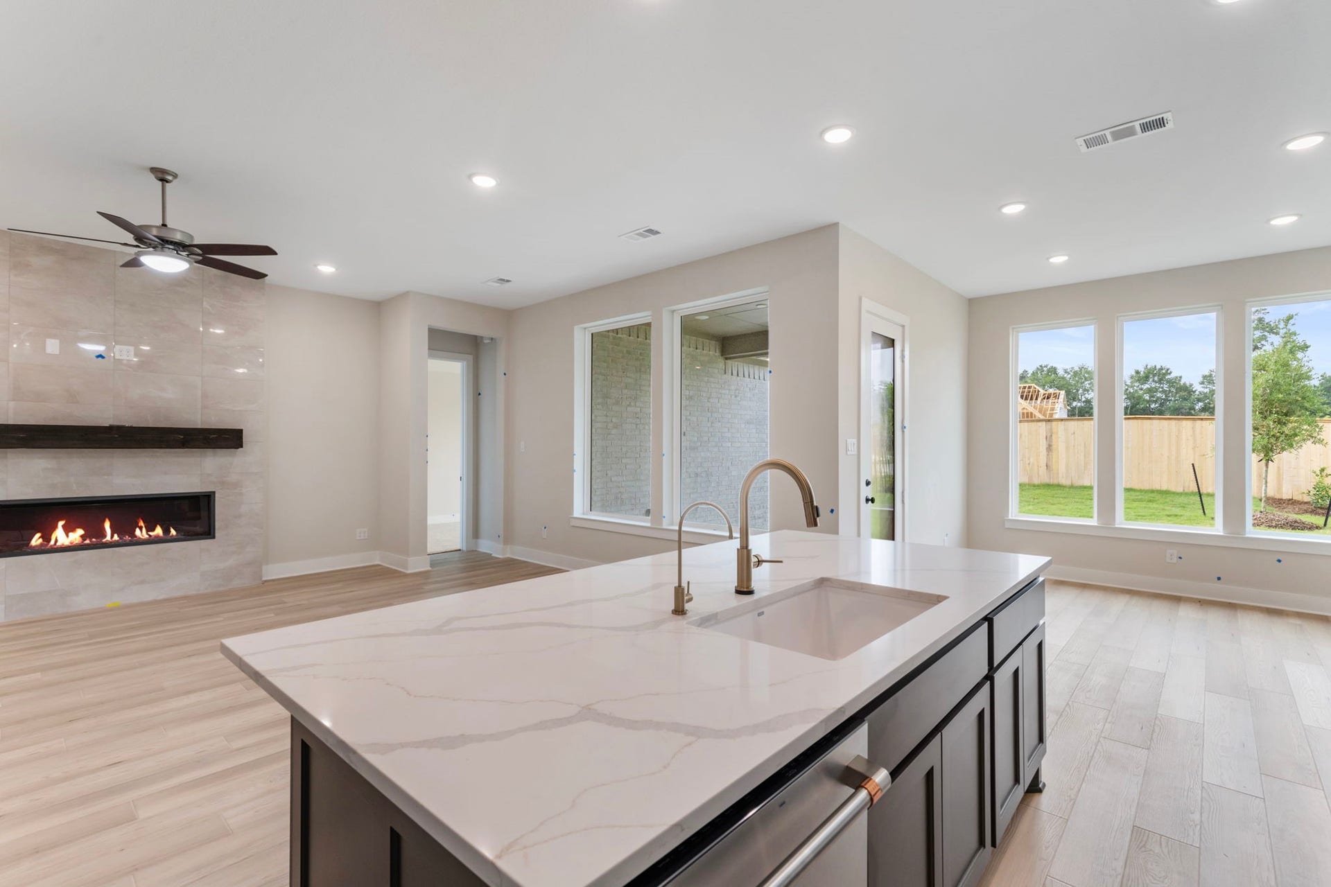 8143 Fenway Heights Dr, The Woodlands, TX 77389 Spacious open-concept living area with the kitchen opening up to the family area, featuring an elegant fireplace, and large windows offering abundant natural light and views of the backyard.