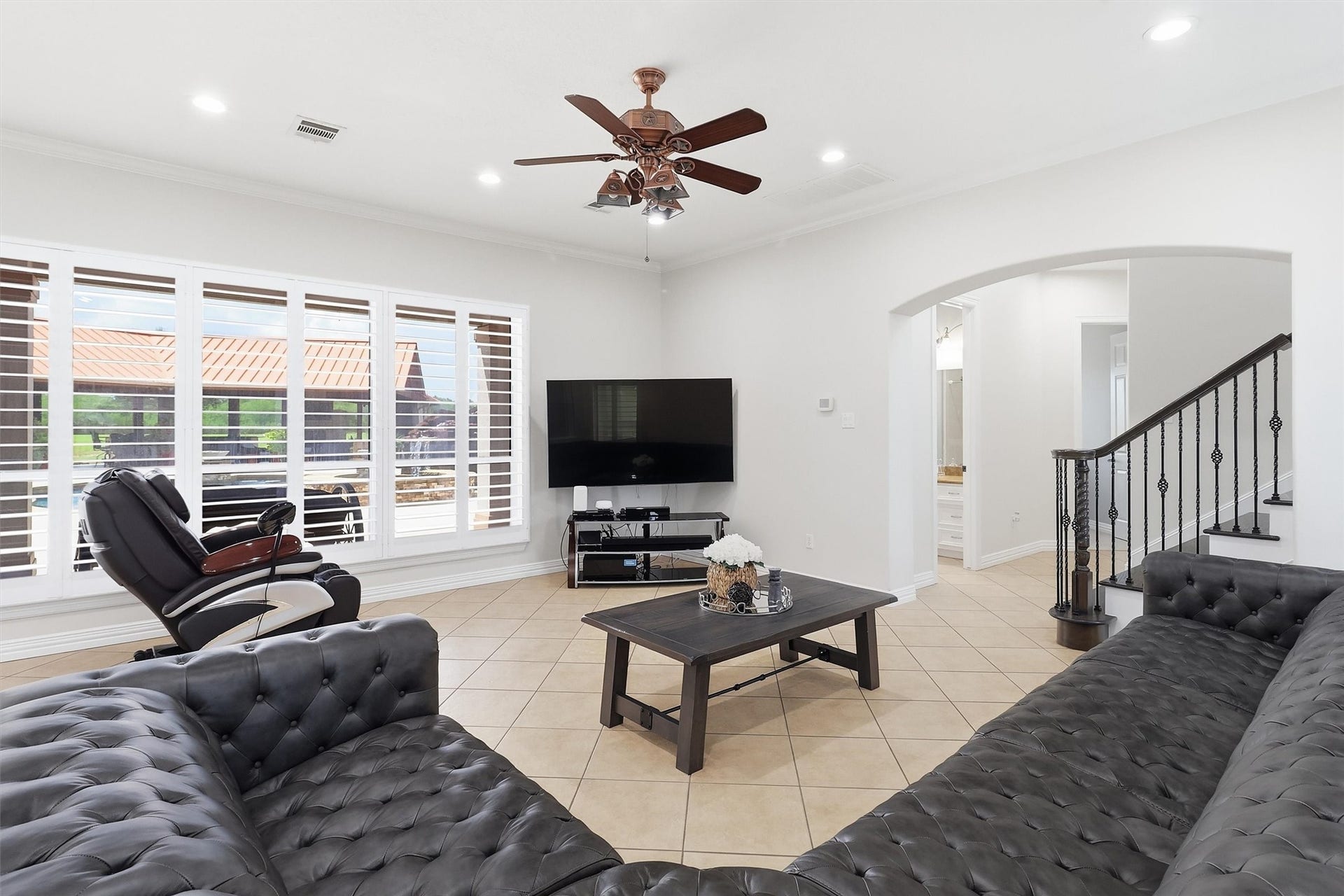 This inviting living space offers tile flooring, plush leather seating, and a large mounted TV. Tucked beside the staircase, it also provides a lovely view of the resort-style pool just outside.