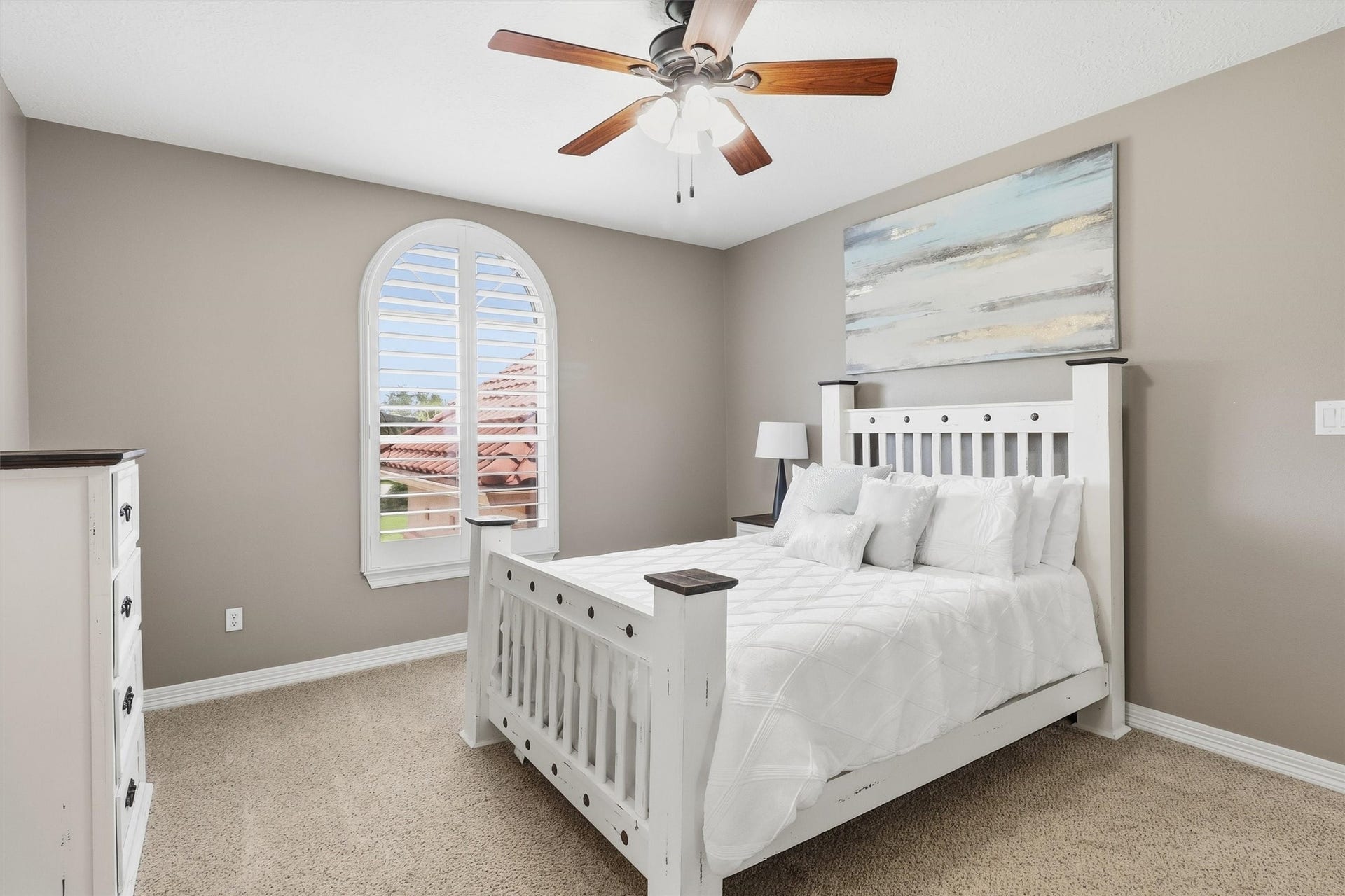 This bright secondary bedroom features an arched window with plantation shutters and neutral carpeting throughout, offering a comfortable and flexible space for guests or loved ones.