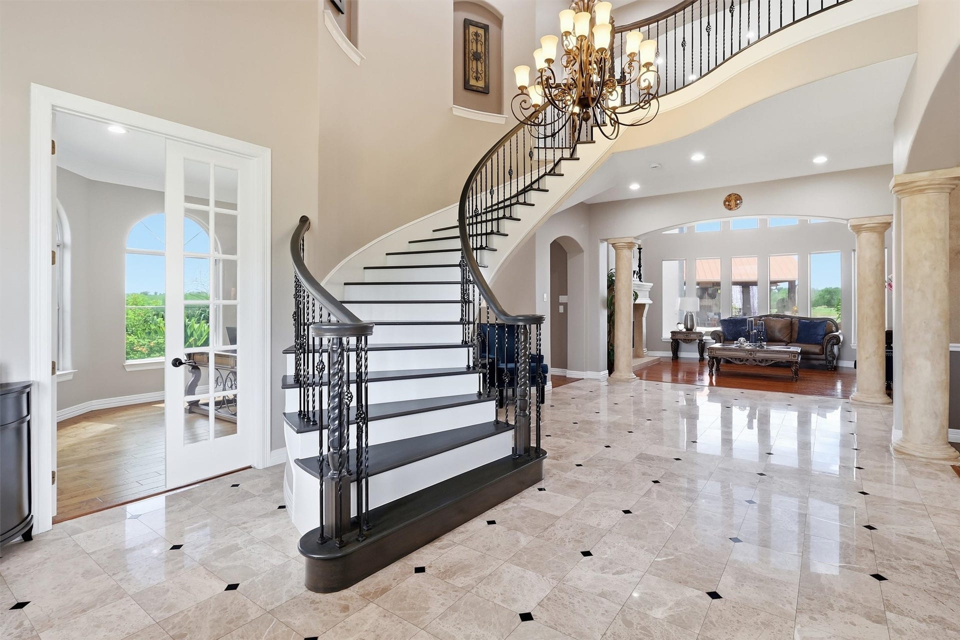 A dramatic curved staircase with wrought iron balusters takes center stage in this two-story entry. Polished tile flooring with diamond inlay accents flows throughout, while an elegant chandelier illuminates the space from above.