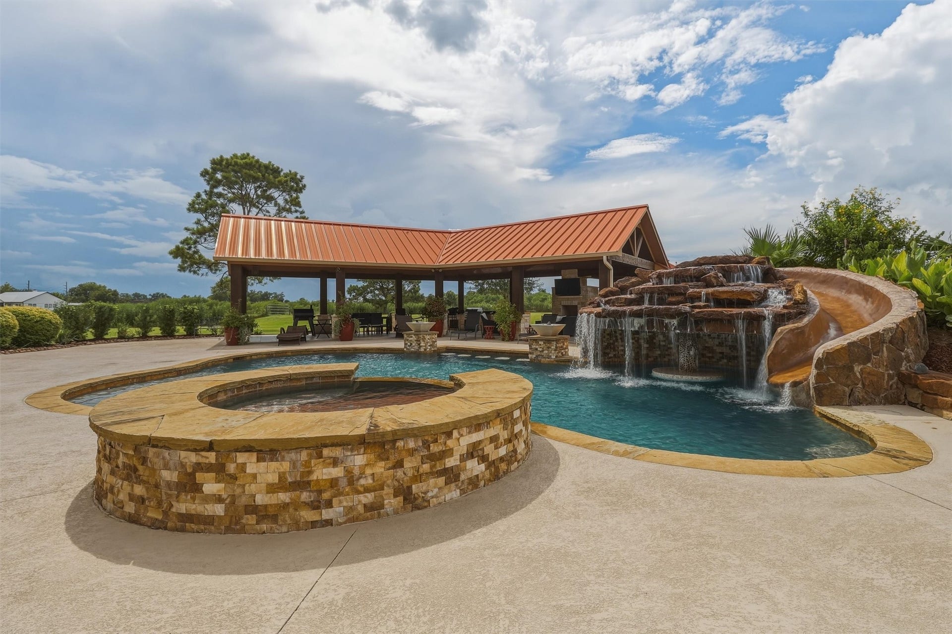 This incredible backyard retreat boasts a free-form pool with a rock waterfall, water slide, and spa, all set against a backdrop of a covered outdoor pavilion, perfect for entertaining loved ones.