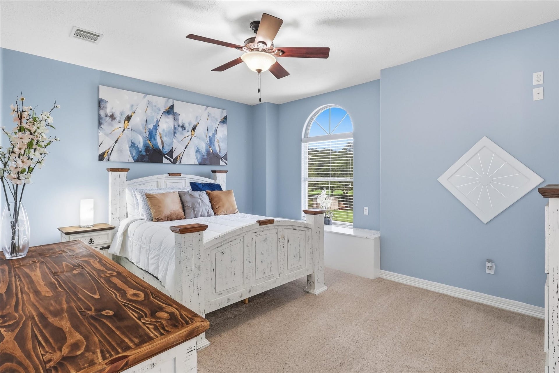 This charming secondary bedroom features soft blue walls, an arched window with picturesque views, and plush carpeting, creating a bright and comfortable retreat.