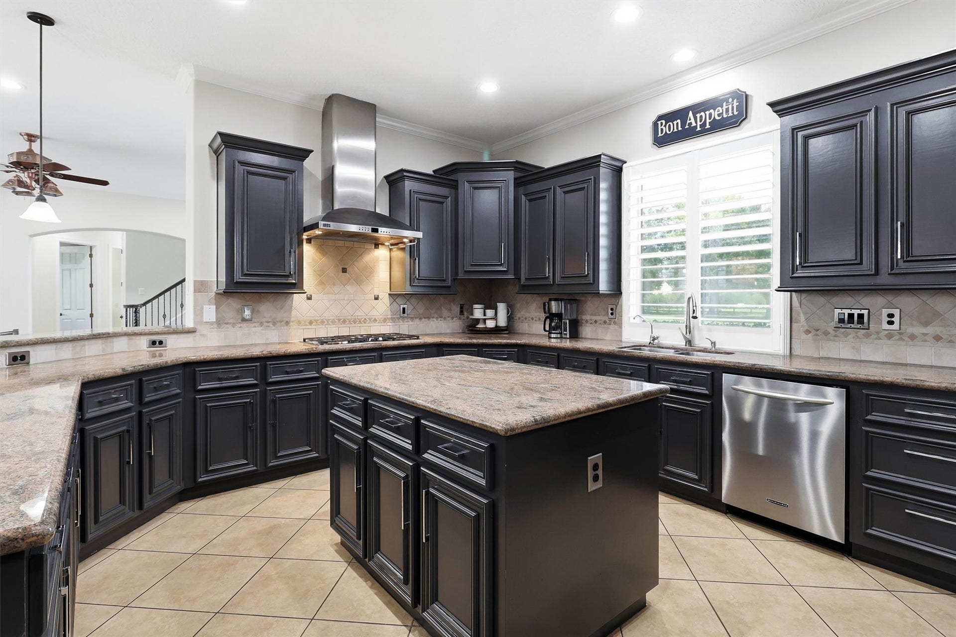 Open-concept gourmet kitchen features rich espresso cabinetry, granite countertops, and a large center island with additional storage. A stainless range hood and gas cooktop make this a chef's delight.
