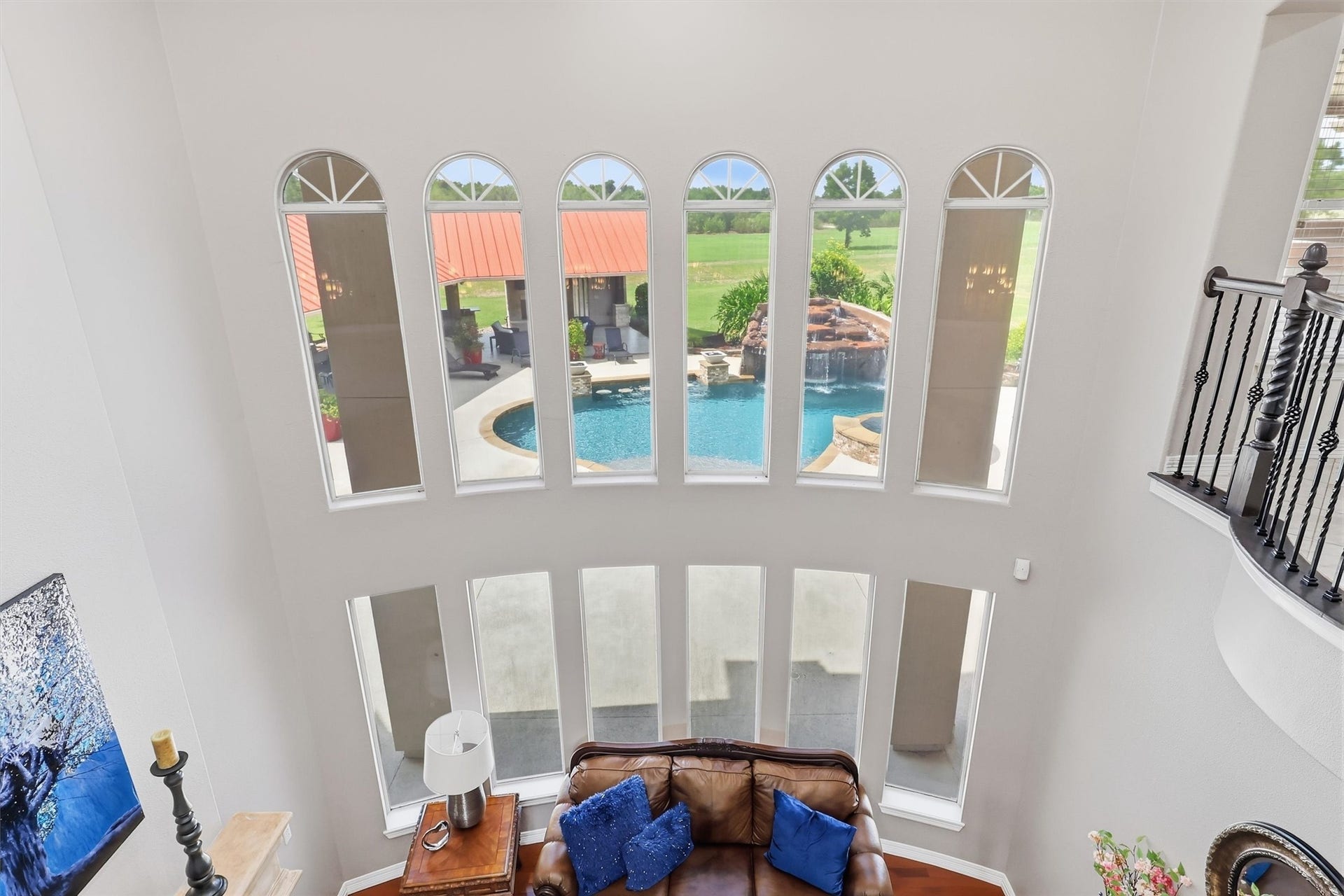 Floor-to-ceiling arched windows showcase a breathtaking view of the resort-style pool, spa, and covered patio beyond. This dramatic architectural feature floods the home with natural light.