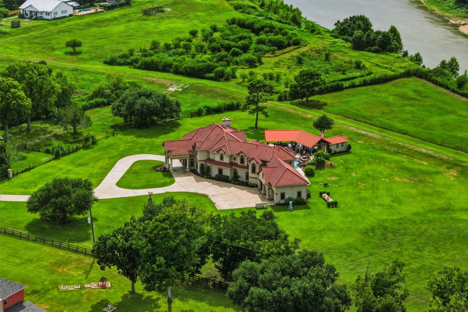 This stunning aerial view showcases the property's picturesque setting, surrounded by lush green pastures and mature trees. The circular driveway and red tile roofline make a lasting first impression.