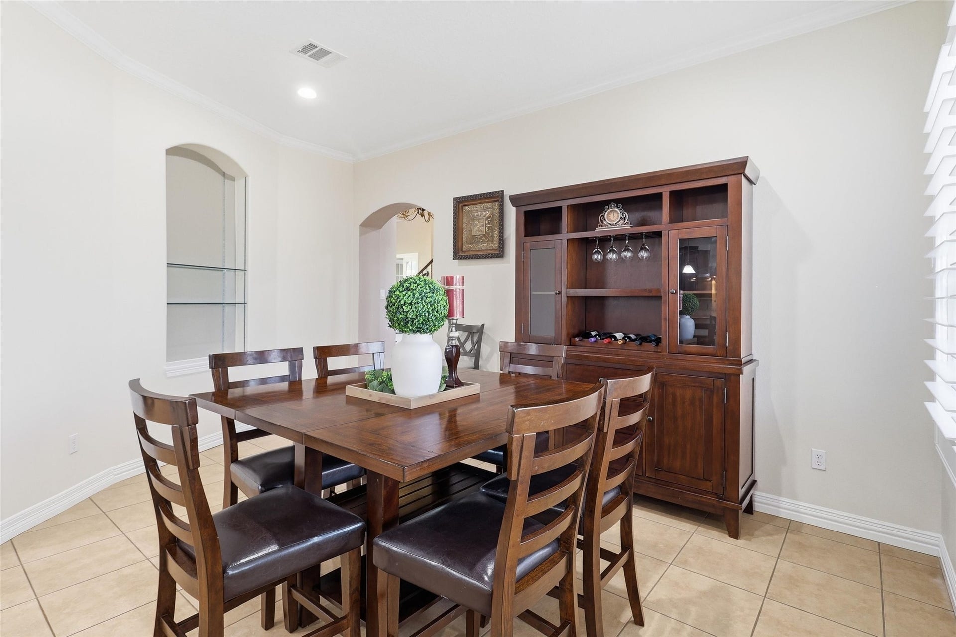 This bright Breakfast area includes a built-in hutch with wine storage and glass-front cabinetry, ideal for entertaining. Tile flooring and an open archway connect seamlessly to the rest of the home.