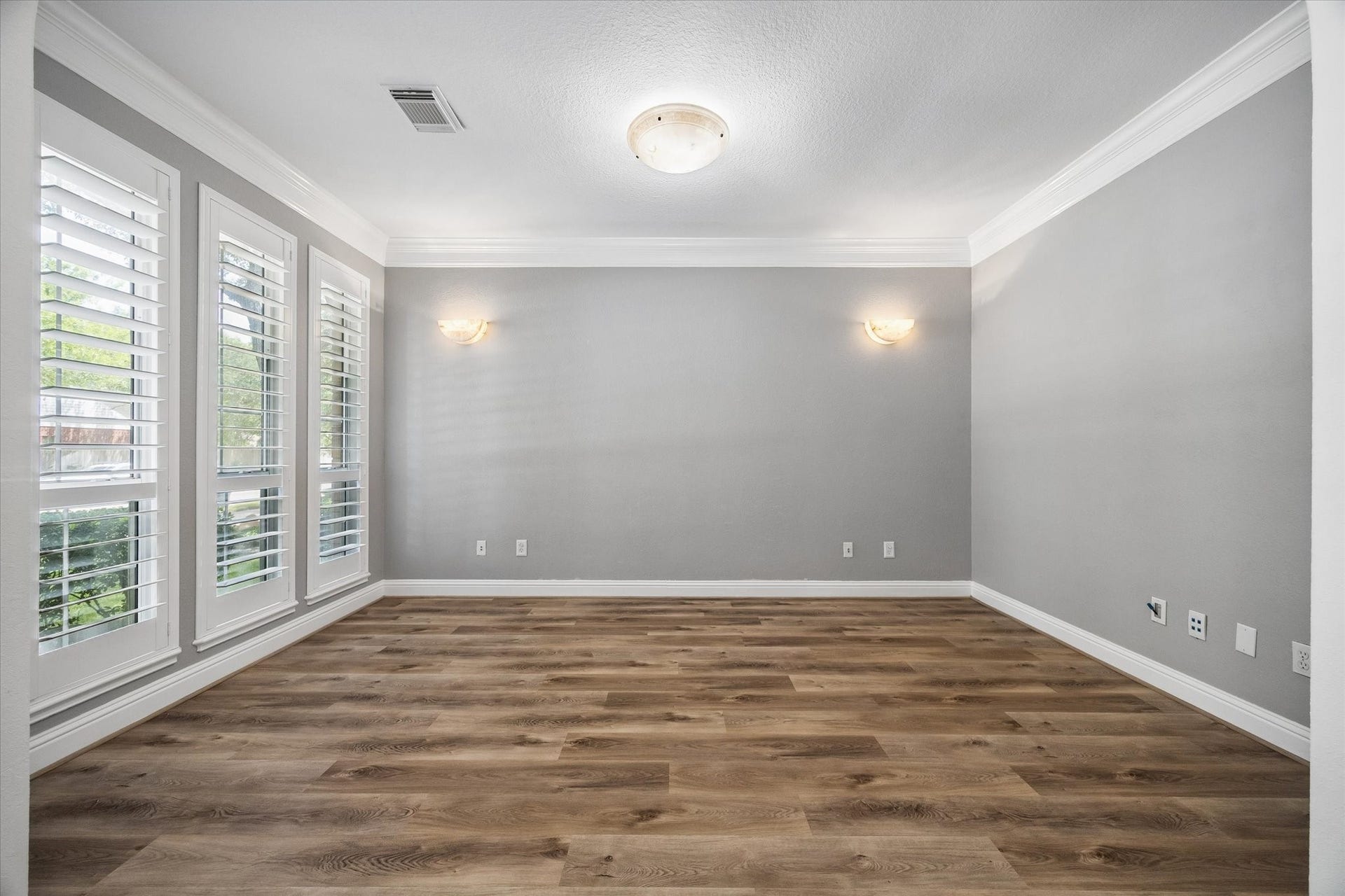 Versatile home office or formal living room featuring custom wood plantation shutters and elegant mounted stone accent lighting that conveys with the home.