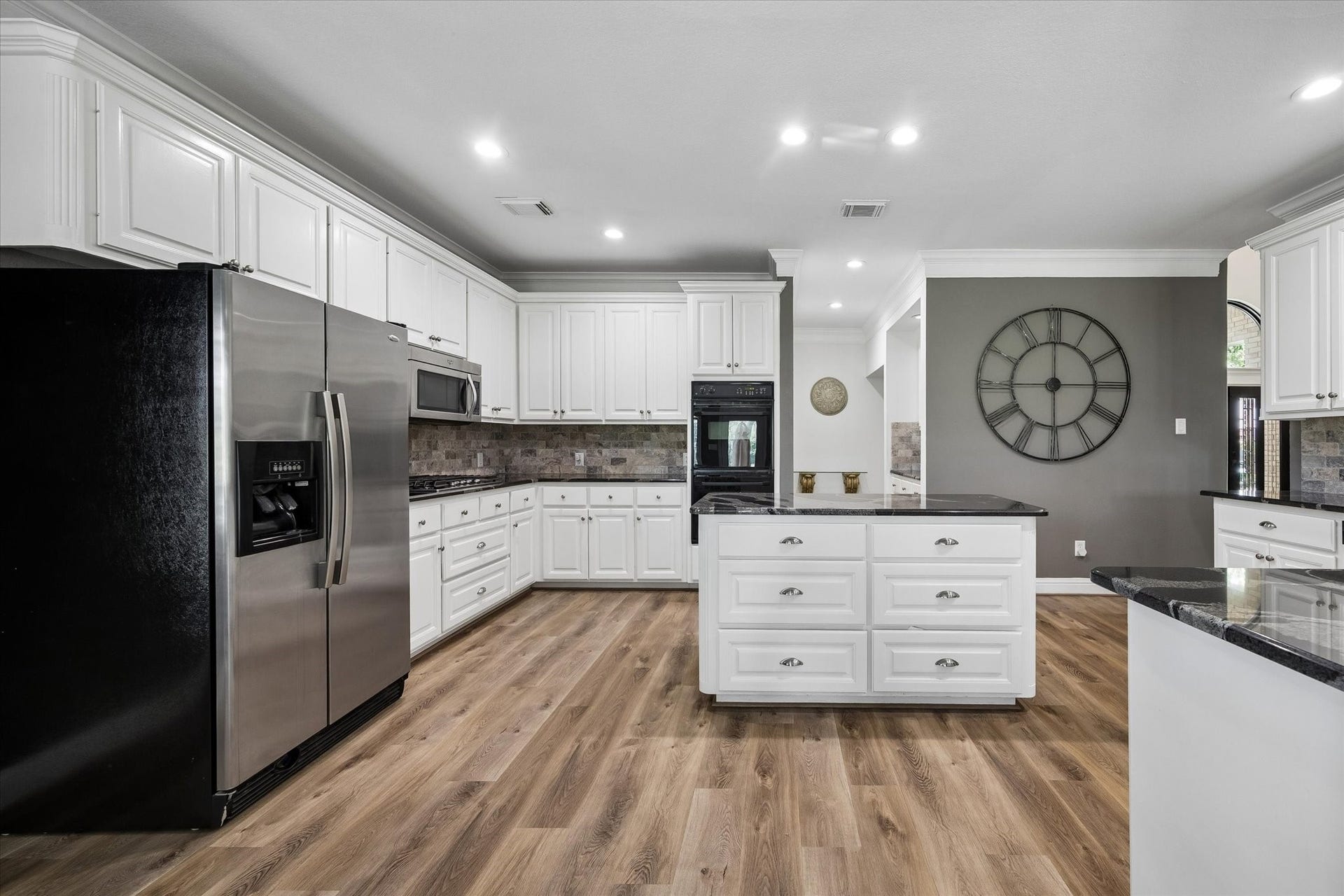 The kitchen features a large center island with a built-in gas cooktop, double ovens, natural stone countertops, and abundant cabinet and storage space.