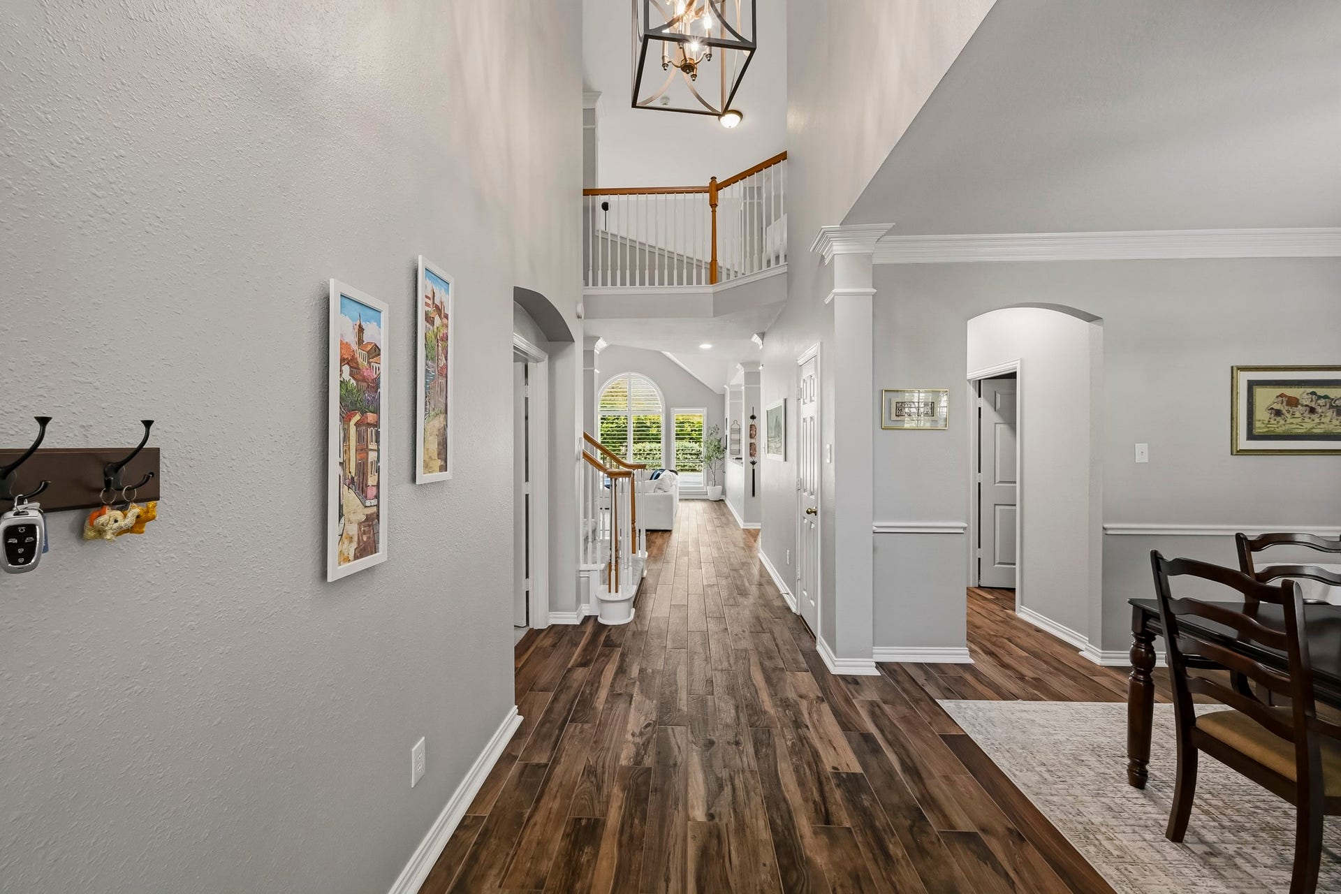 5702 Misty Island Court, Katy, TX 77494 Elegant entryway with rich wood flooring, high ceilings, and tasteful wall art leads to a bright living space. A dining area is visible, showcasing classic design and warm tones.