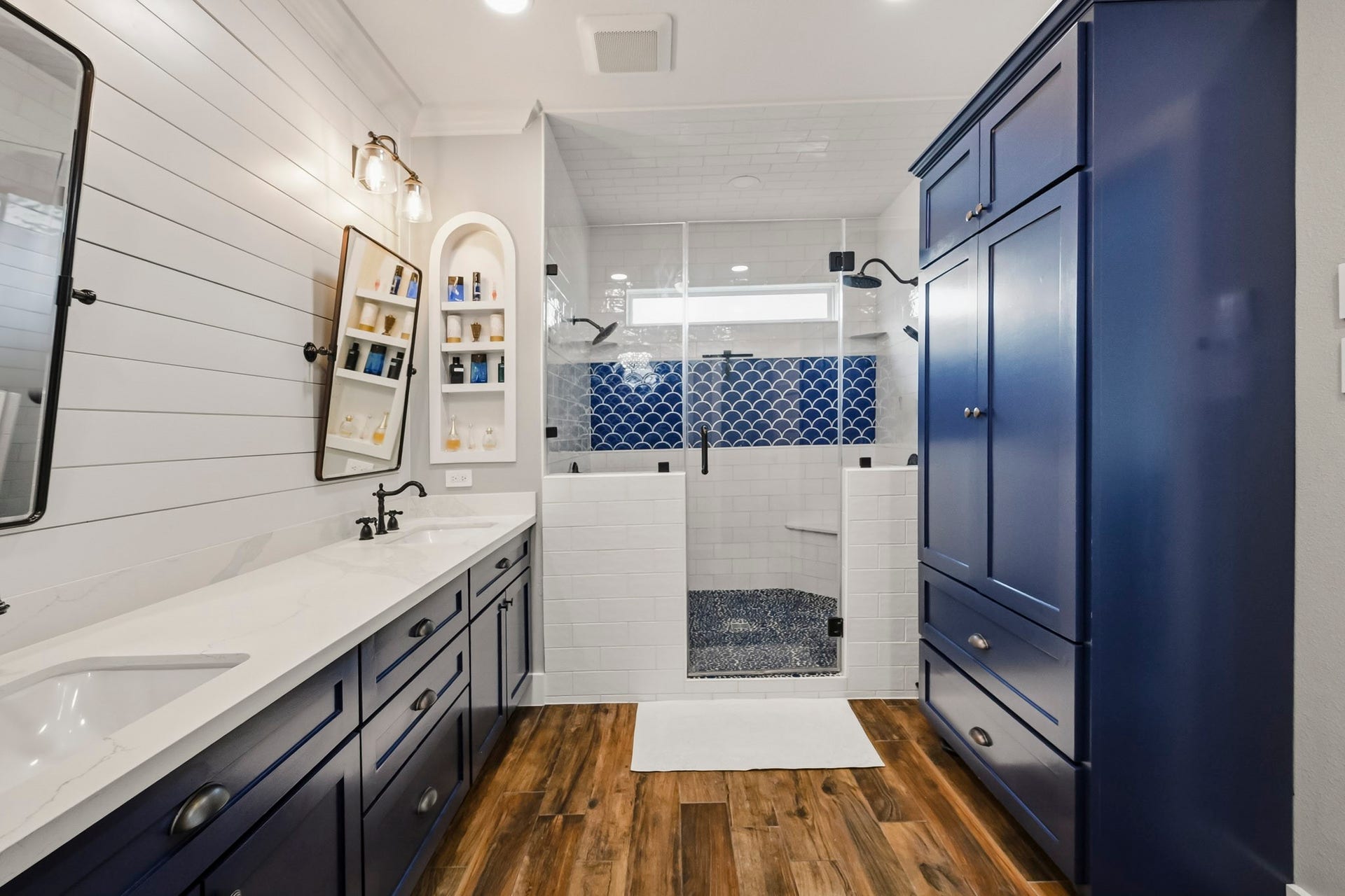5702 Misty Island Court, Katy, TX 77494 Experience modern elegance in this bathroom featuring a spacious walk-in shower with eye-catching blue tile accents and sleek glass doors. The rich blue cabinetry complements the warm wood flooring, while the dual sinks and stylish lighting enhance functionality and charm.