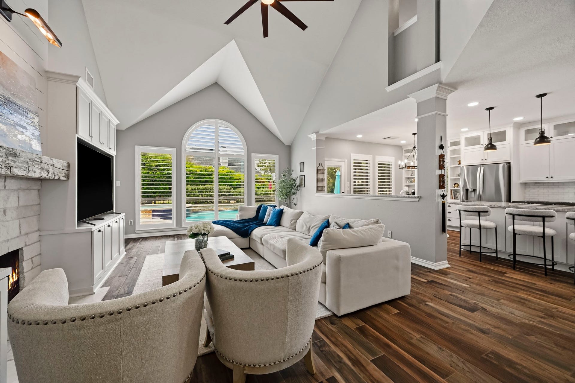 5702 Misty Island Court, Katy, TX 77494 Spacious living area with vaulted ceilings and abundant natural light, featuring a cozy fireplace and views of the pool. The open layout seamlessly connects to a modern kitchen with a breakfast bar, creating an inviting space for relaxation and entertaining.