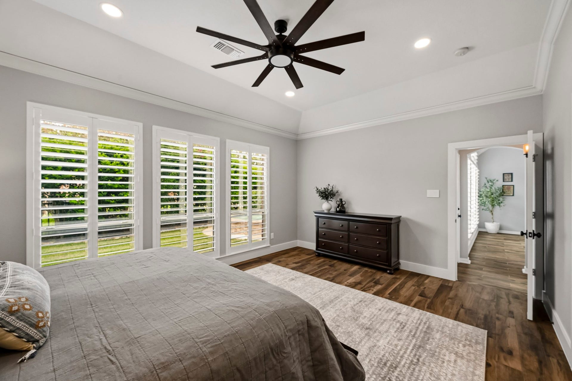 5702 Misty Island Court, Katy, TX 77494 Spacious bedroom featuring elegant wood flooring, abundant natural light from large windows with shutters, and a modern ceiling fan.