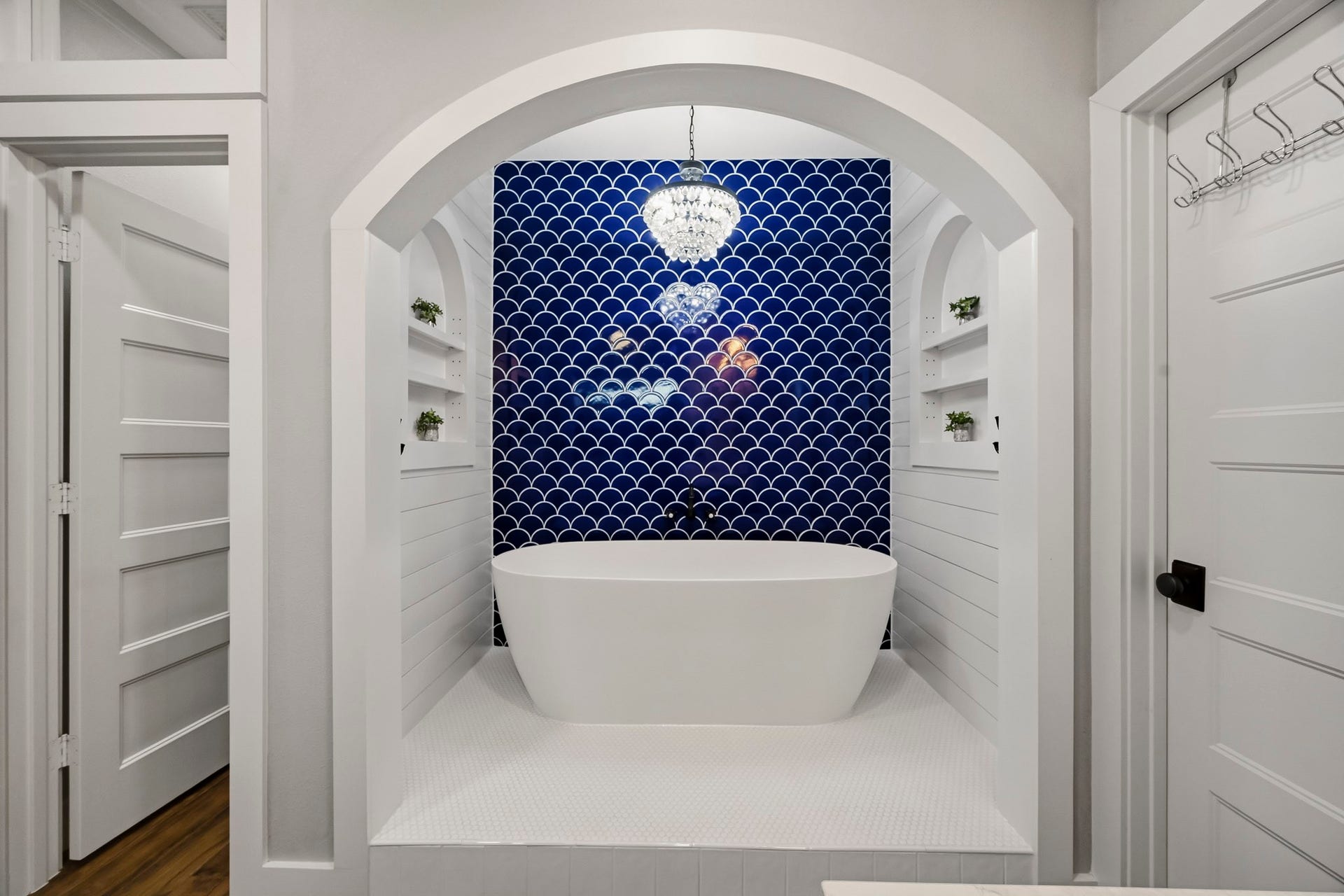 5702 Misty Island Court, Katy, TX 77494 Luxurious bathroom featuring a freestanding soaking tub set against a striking blue tiled wall, complemented by elegant built-in shelving and a chic chandelier.