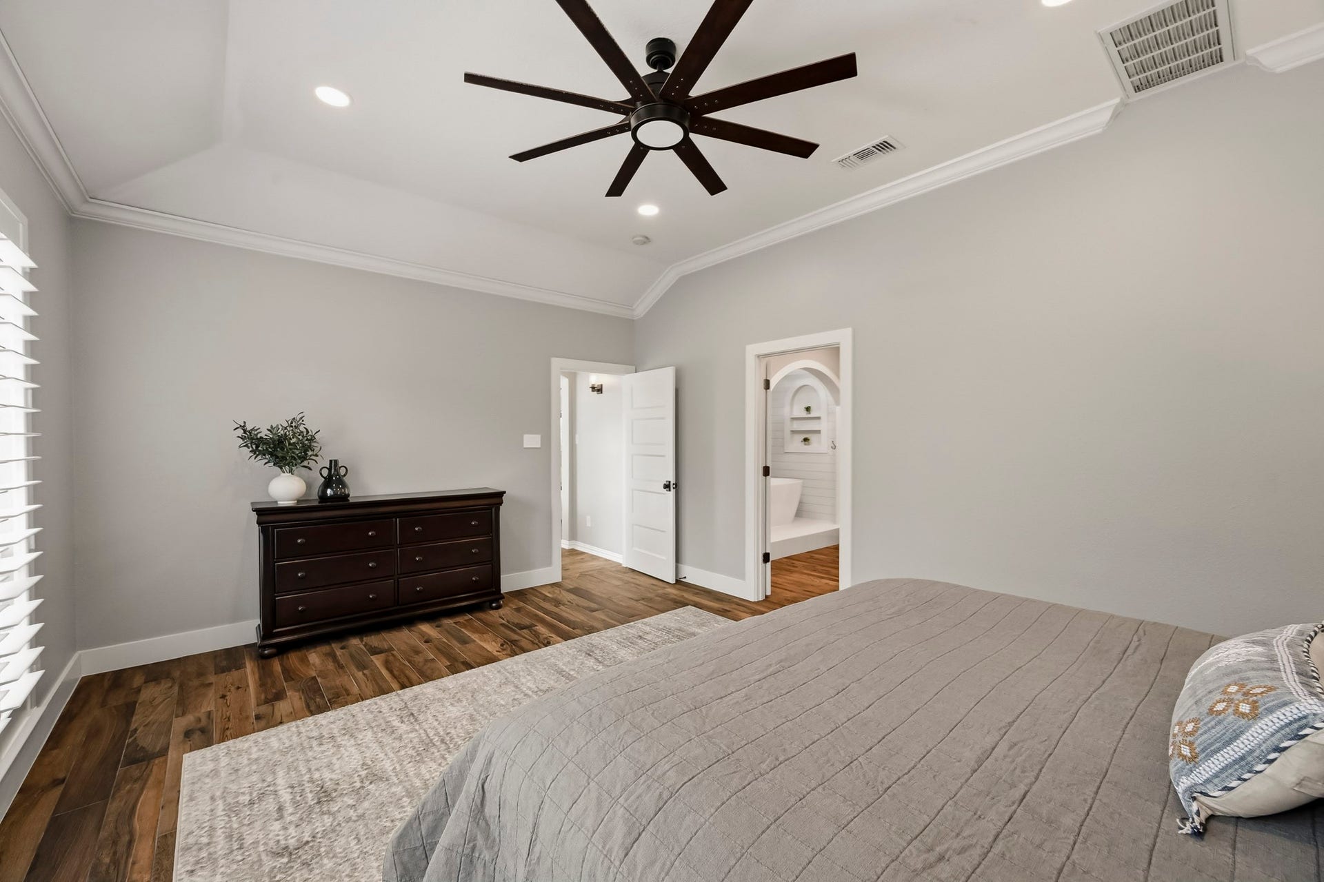 5702 Misty Island Court, Katy, TX 77494 Spacious bedroom with elegant hardwood floors, a modern ceiling fan, and a soothing neutral palette. Natural light streams through large windows, highlighting the stylish dresser and providing a seamless flow into a chic en-suite bathroom.