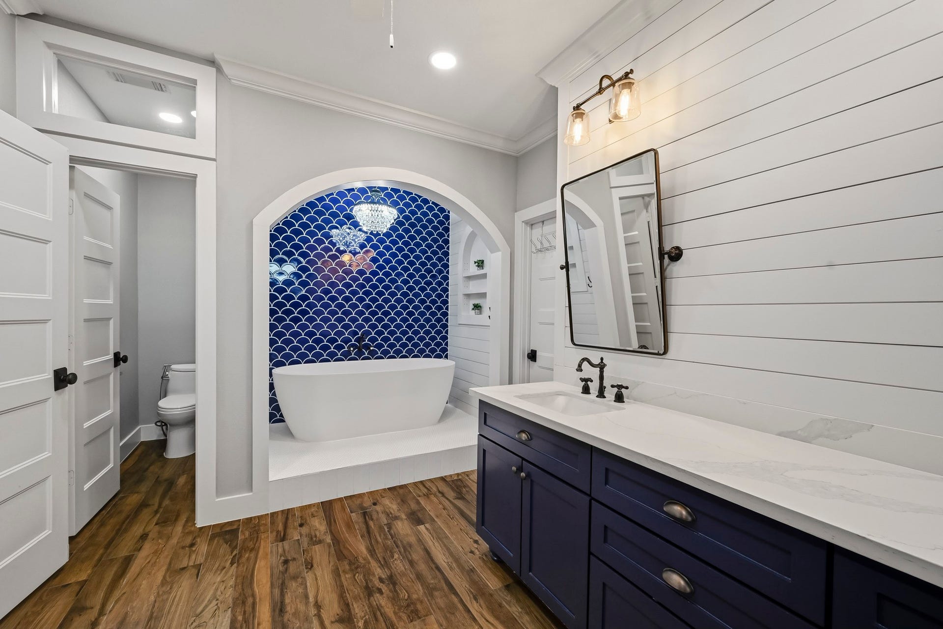 5702 Misty Island Court, Katy, TX 77494 Elegant bathroom featuring a freestanding tub set against a striking blue tile accent wall, complemented by a chic double vanity with modern fixtures and warm wood flooring.
