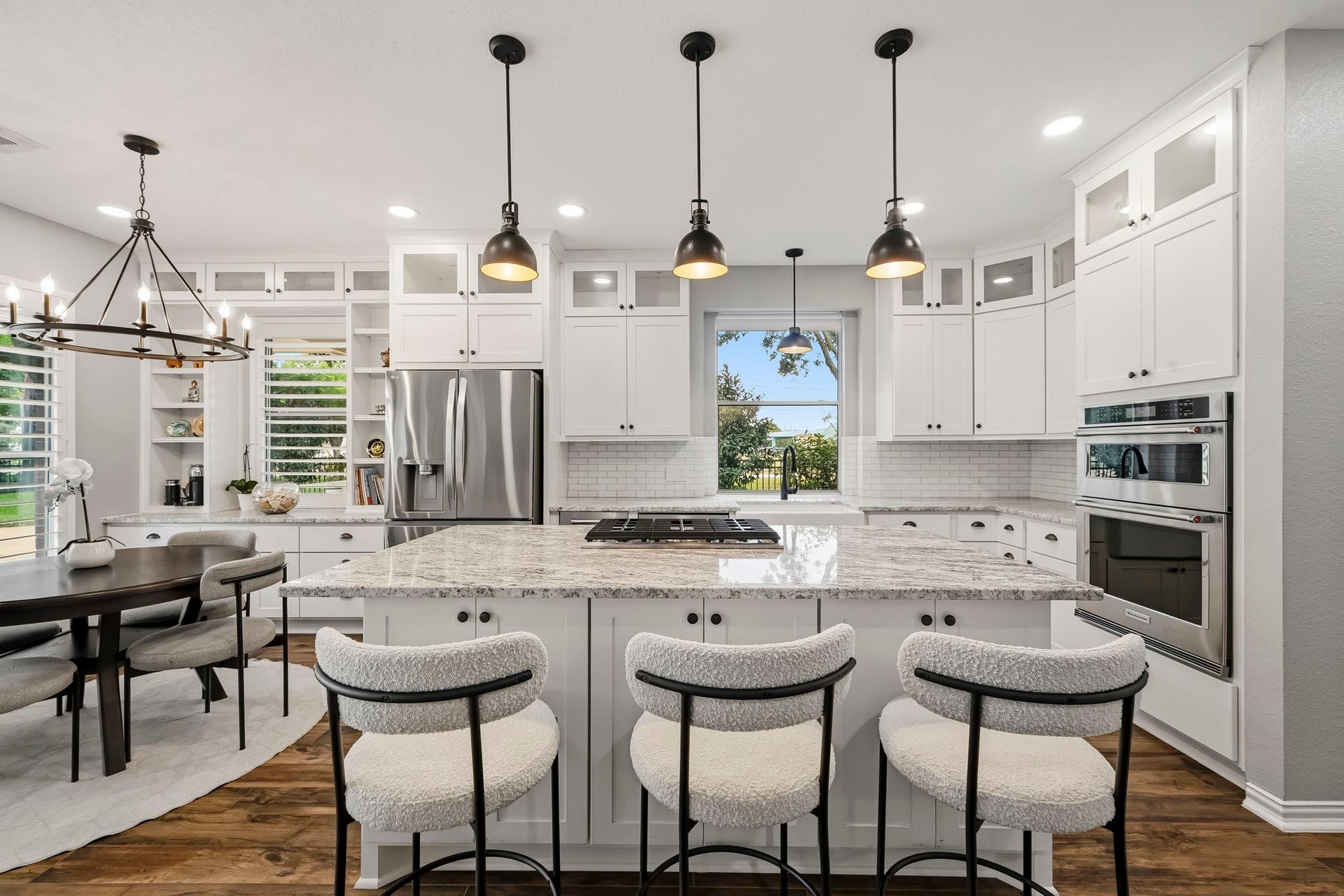 5702 Misty Island Court, Katy, TX 77494 A modern kitchen featuring a large marble island with seating, elegant pendant lighting, and sleek stainless steel appliances. The open layout seamlessly connects to a cozy dining area, enhanced by abundant natural light and stylish cabinetry.