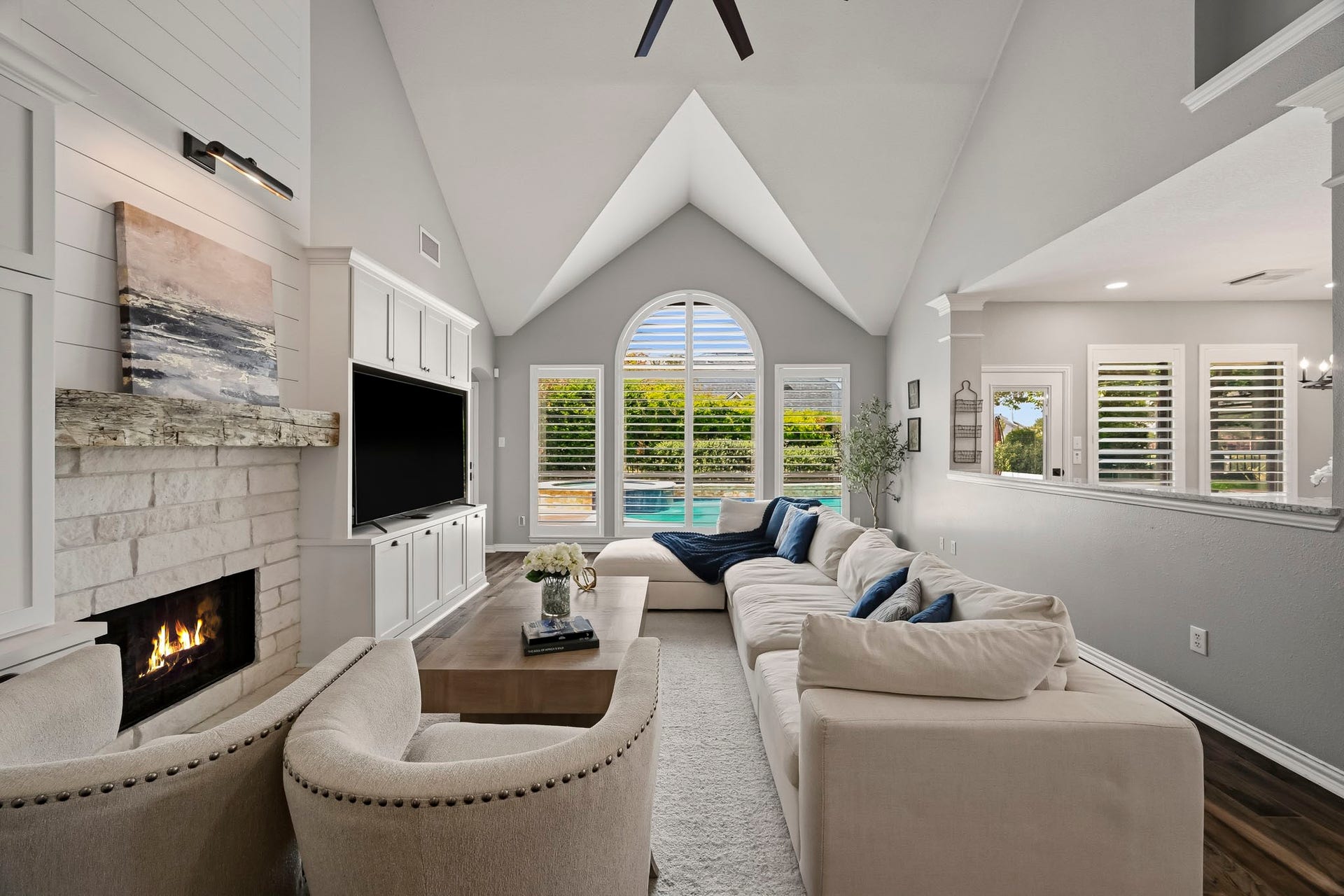 5702 Misty Island Court, Katy, TX 77494 Spacious living room featuring a vaulted ceiling, cozy fireplace, and large arched windows framing a view of the pool.