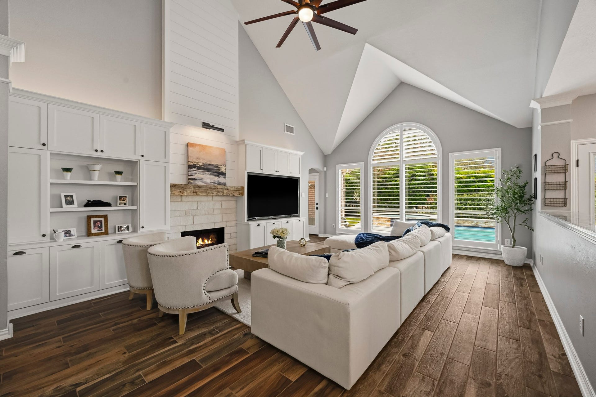 5702 Misty Island Court, Katy, TX 77494 Spacious living room with vaulted ceilings, abundant natural light from large arched windows, elegant hardwood floors, and a cozy fireplace, perfect for relaxation and entertaining.