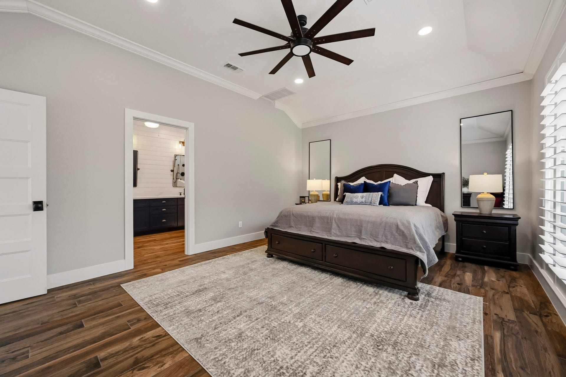 5702 Misty Island Court, Katy, TX 77494 Spacious primary bedroom with elegant wood flooring, a large ceiling fan, and abundant natural light. Features a cozy bed with plush bedding, dual nightstands, and direct access to a stylish en-suite bathroom.