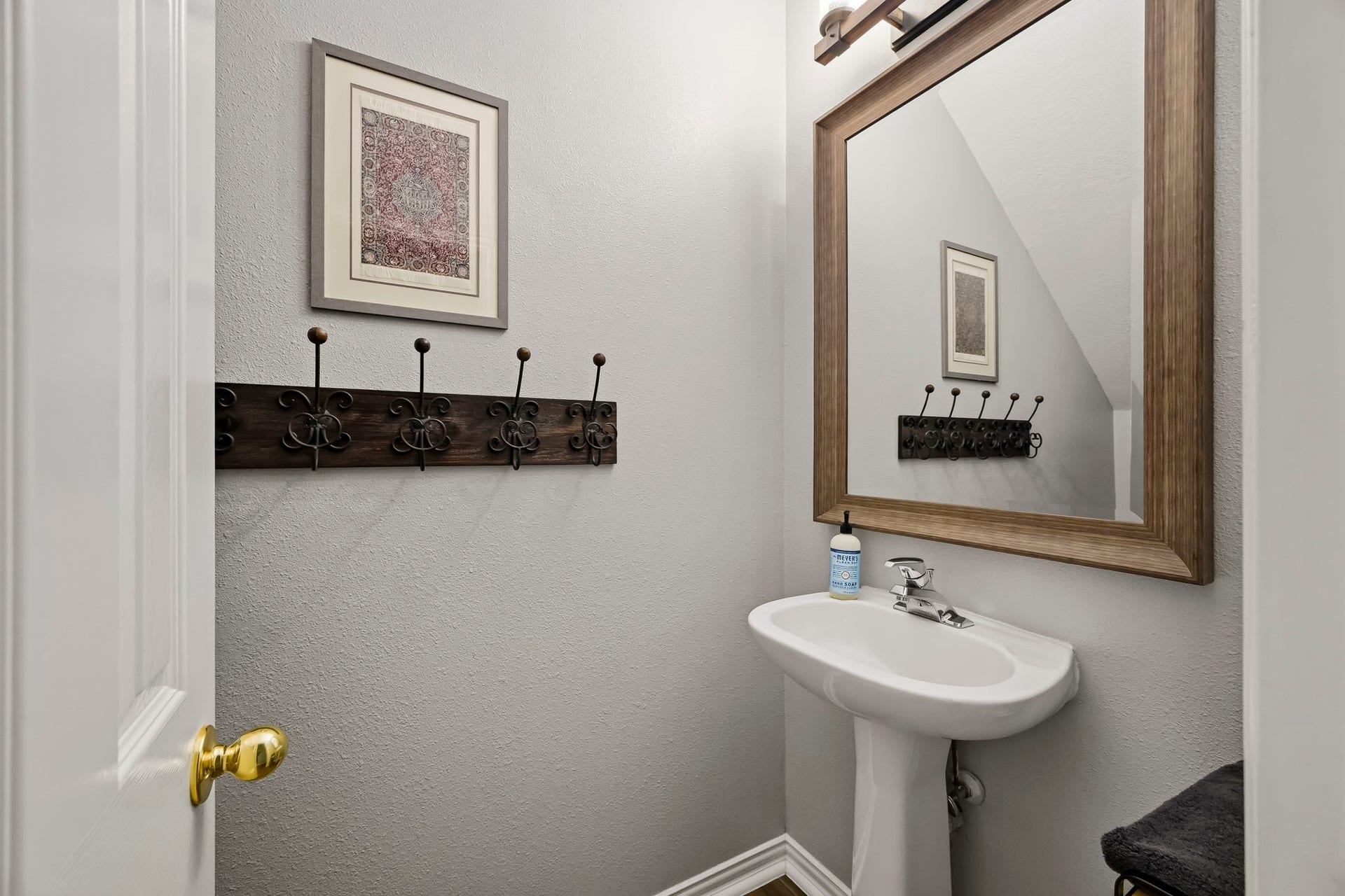 5702 Misty Island Court, Katy, TX 77494 Charming powder room with a sleek pedestal sink, elegant framed mirror, and stylish wall hooks, perfect for guests.