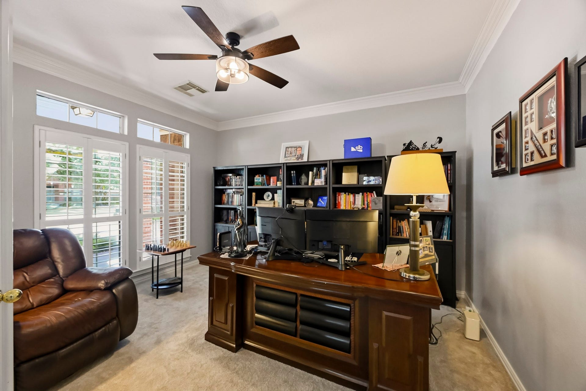 5702 Misty Island Court, Katy, TX 77494 A bright and inviting home office features large windows with elegant shutters, built-in shelving, and a spacious desk area, perfect for productivity and comfort.