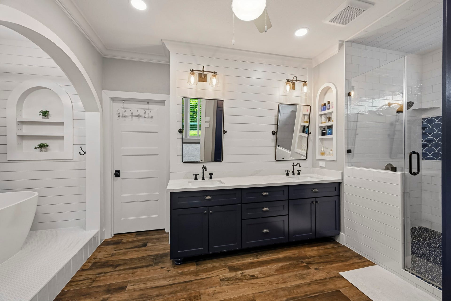 5702 Misty Island Court, Katy, TX 77494 Elegant bathroom featuring a double vanity with sleek black fixtures, a spacious glass-enclosed shower, and a luxurious freestanding tub, all enhanced by chic shiplap walls and warm wood flooring.