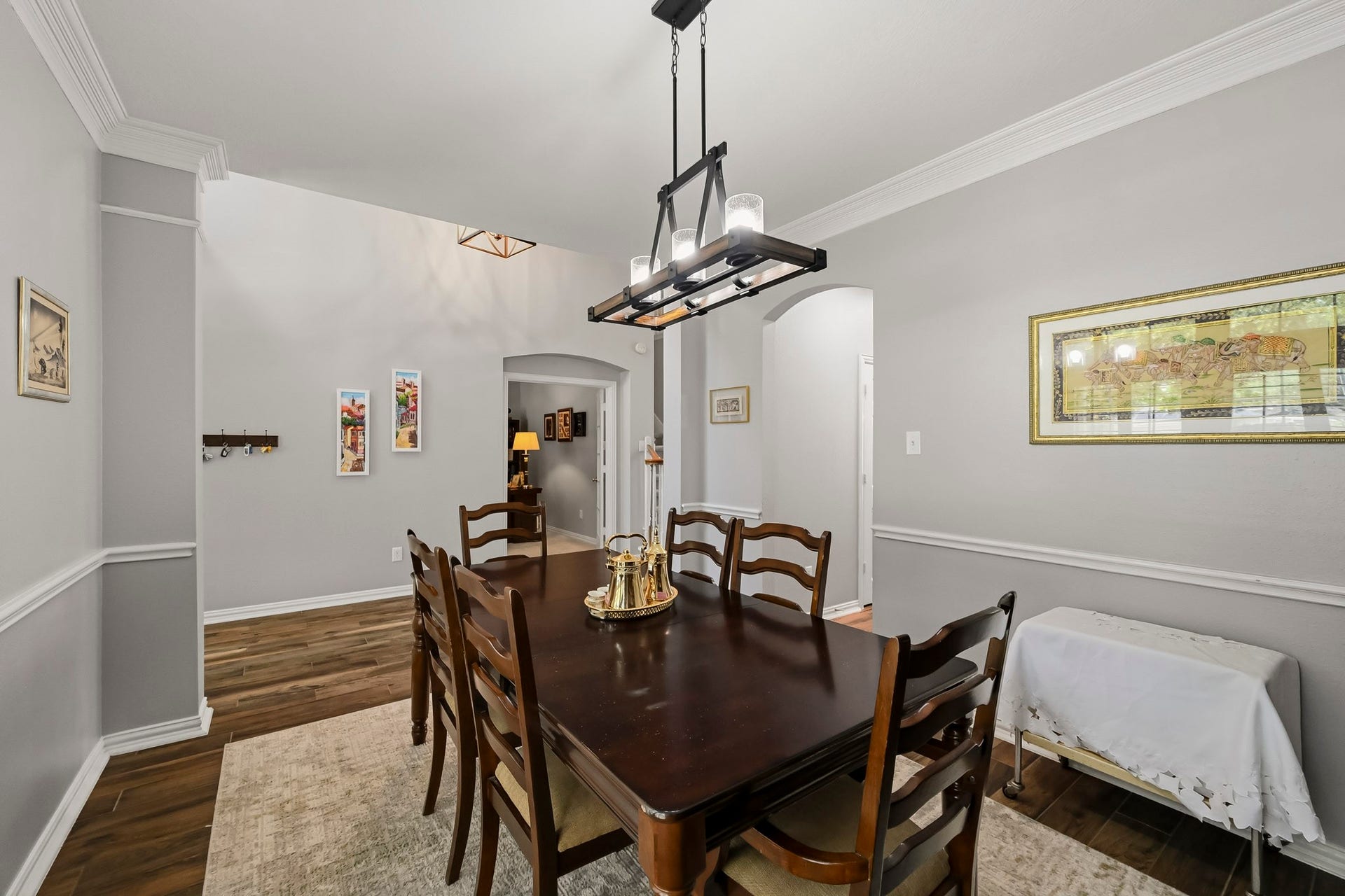 5702 Misty Island Court, Katy, TX 77494 Elegant dining room featuring a long wooden table with matching chairs, complemented by a modern chandelier. The room is accented with crown molding, neutral walls, and tasteful artwork, creating a warm and inviting atmosphere.