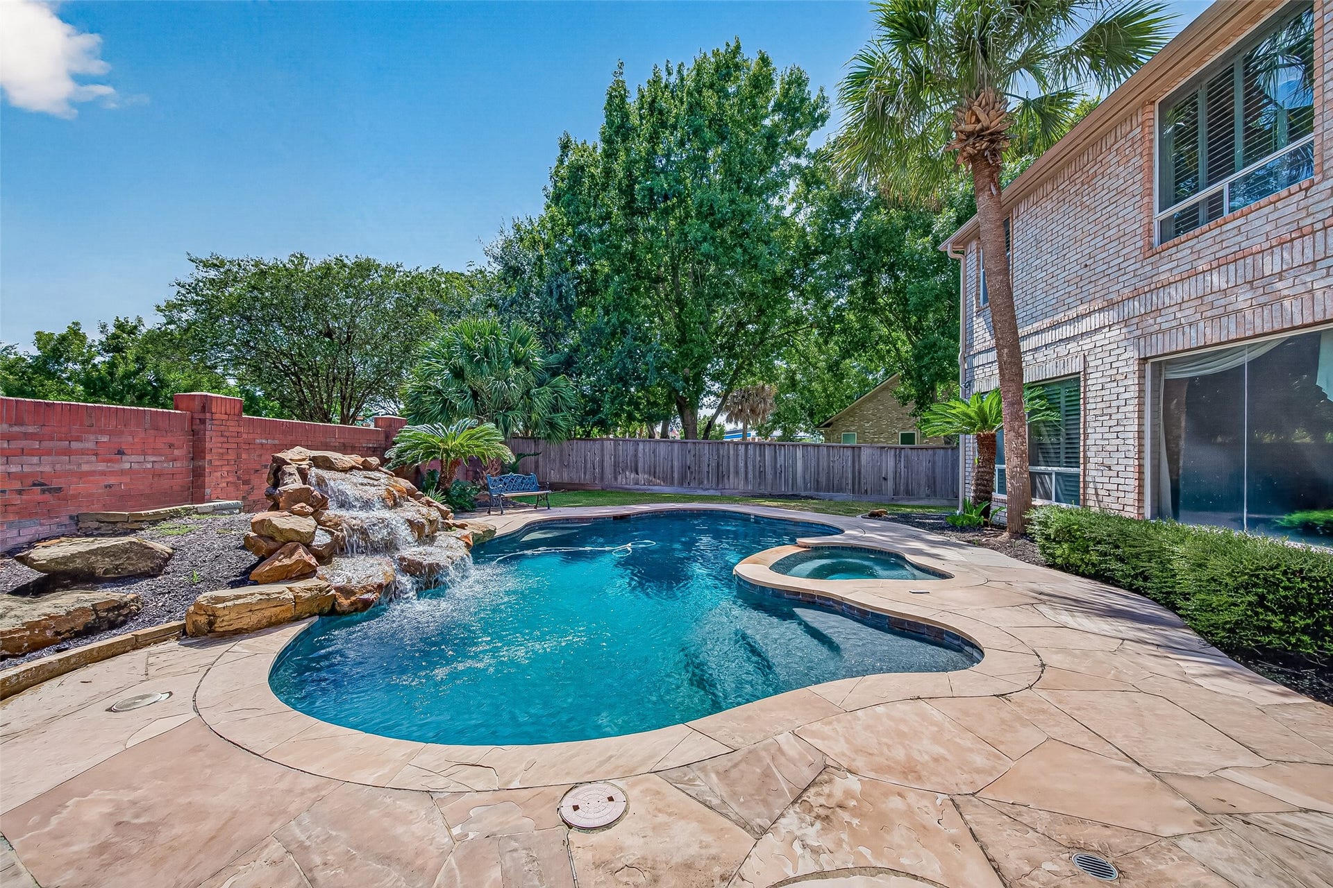 63 Harbor View Drive, Sugar Land, TX 77479 A stunning backyard oasis featuring a sparkling pool with a cascading waterfall, surrounded by lush landscaping and ample patio space for relaxing or entertaining.