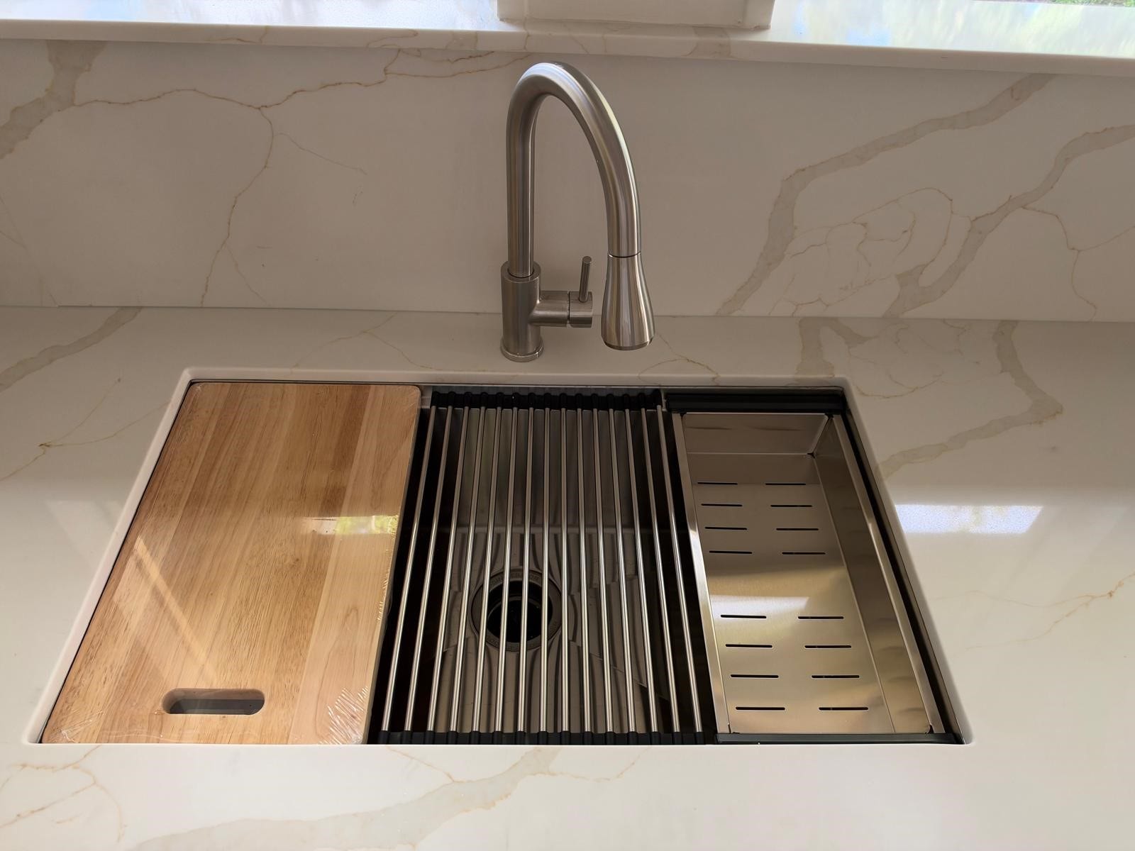 Kitchen features a workstation sink with cutting board. Roll-up drying rack and colander.