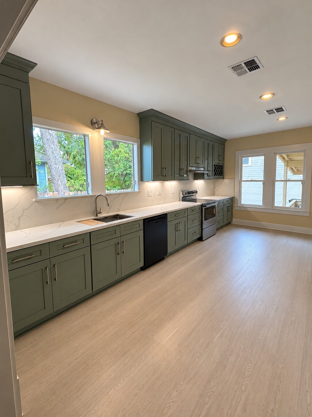 Beautifully remodeled in 2026, this kitchen showcases sage green shaker-style cabinetry, elegant white countertops with subtle veining, coordinating backsplash, updated fixtures, and abundant natural light.