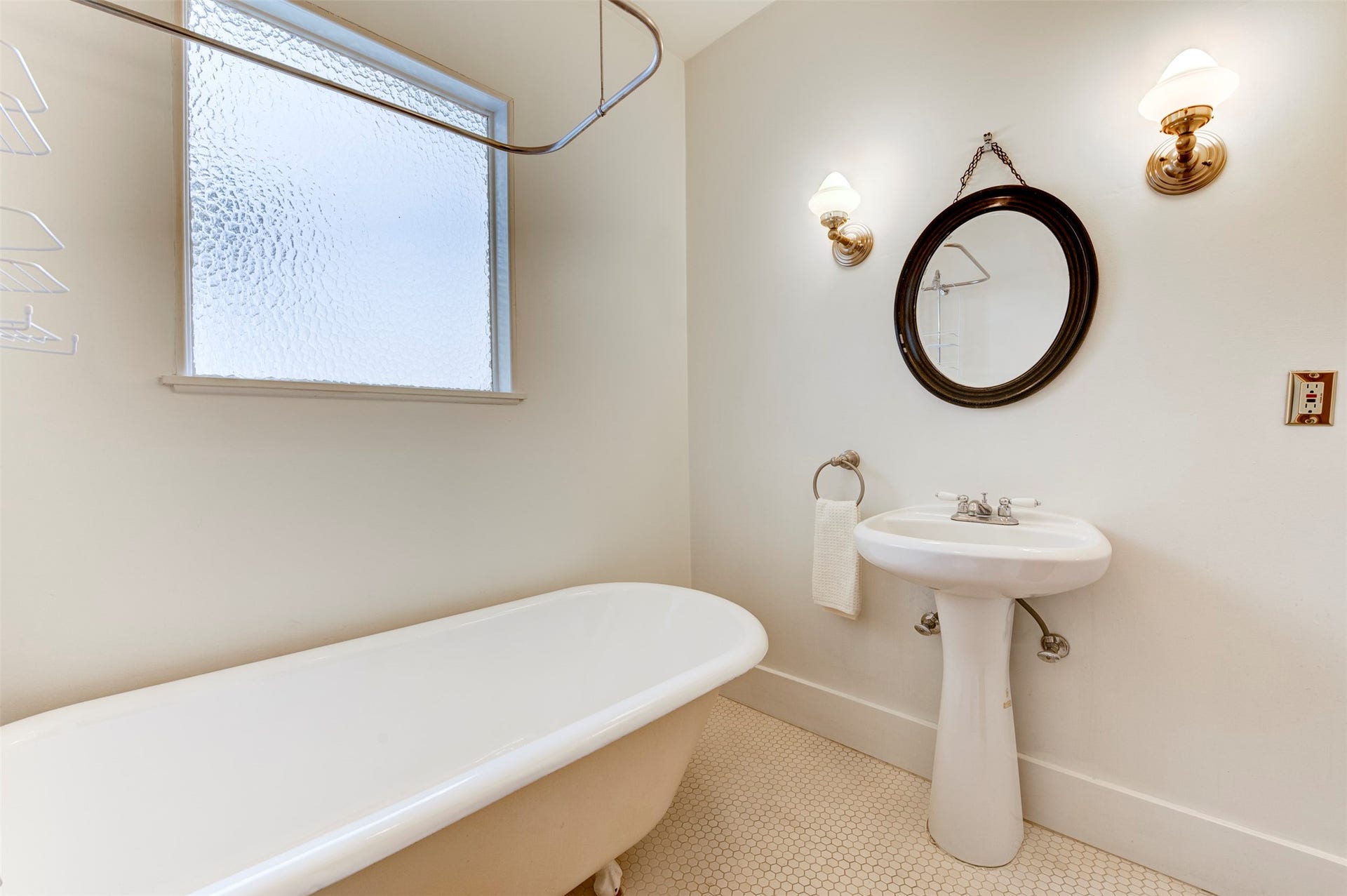 An antique clawfoot tub, vintage brass wall sconce and hex tile come together for to create timeless charm.