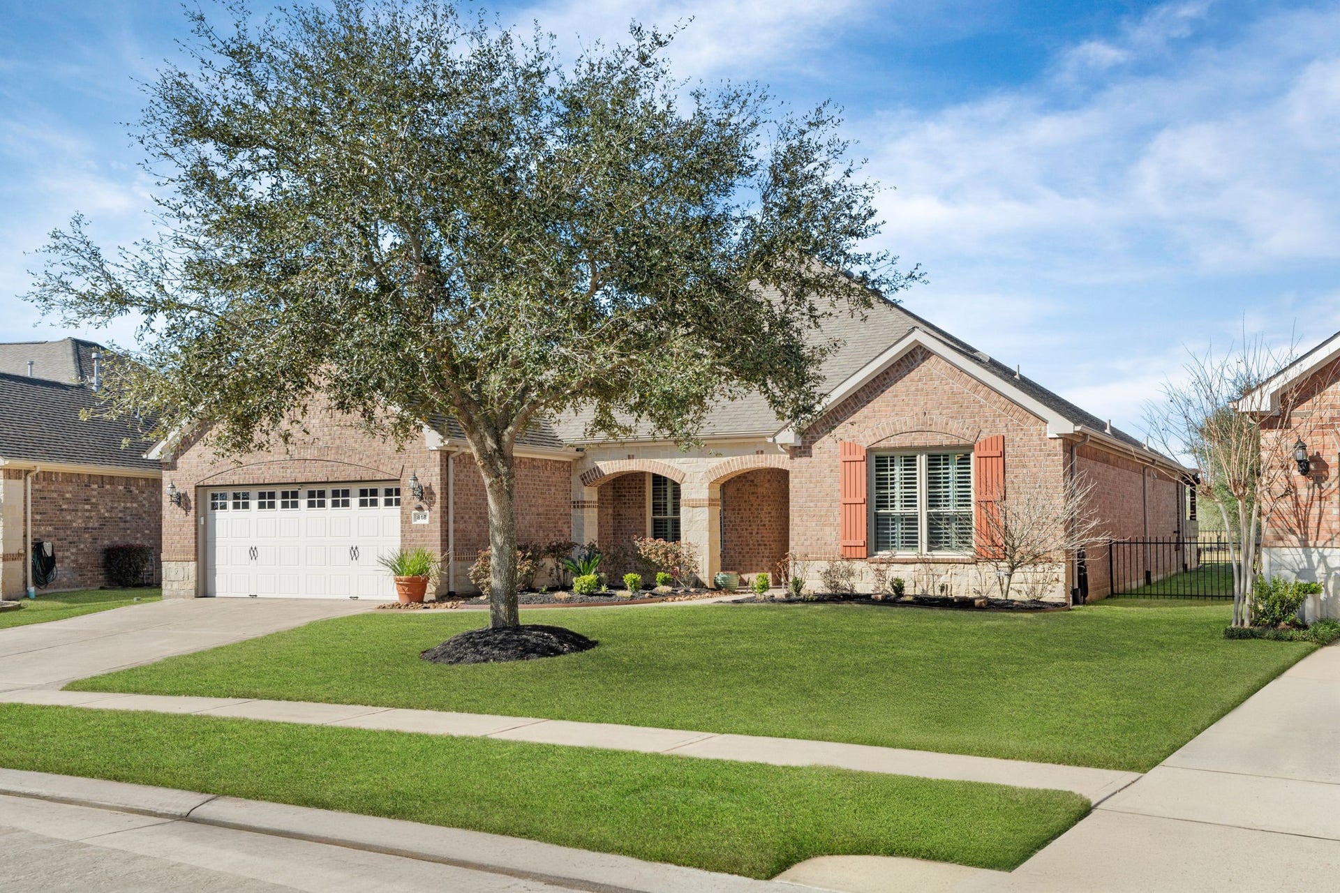 Lovely single-story home with a stone facade and arched entryway, complemented by mature shrubs and a manicured lawn.