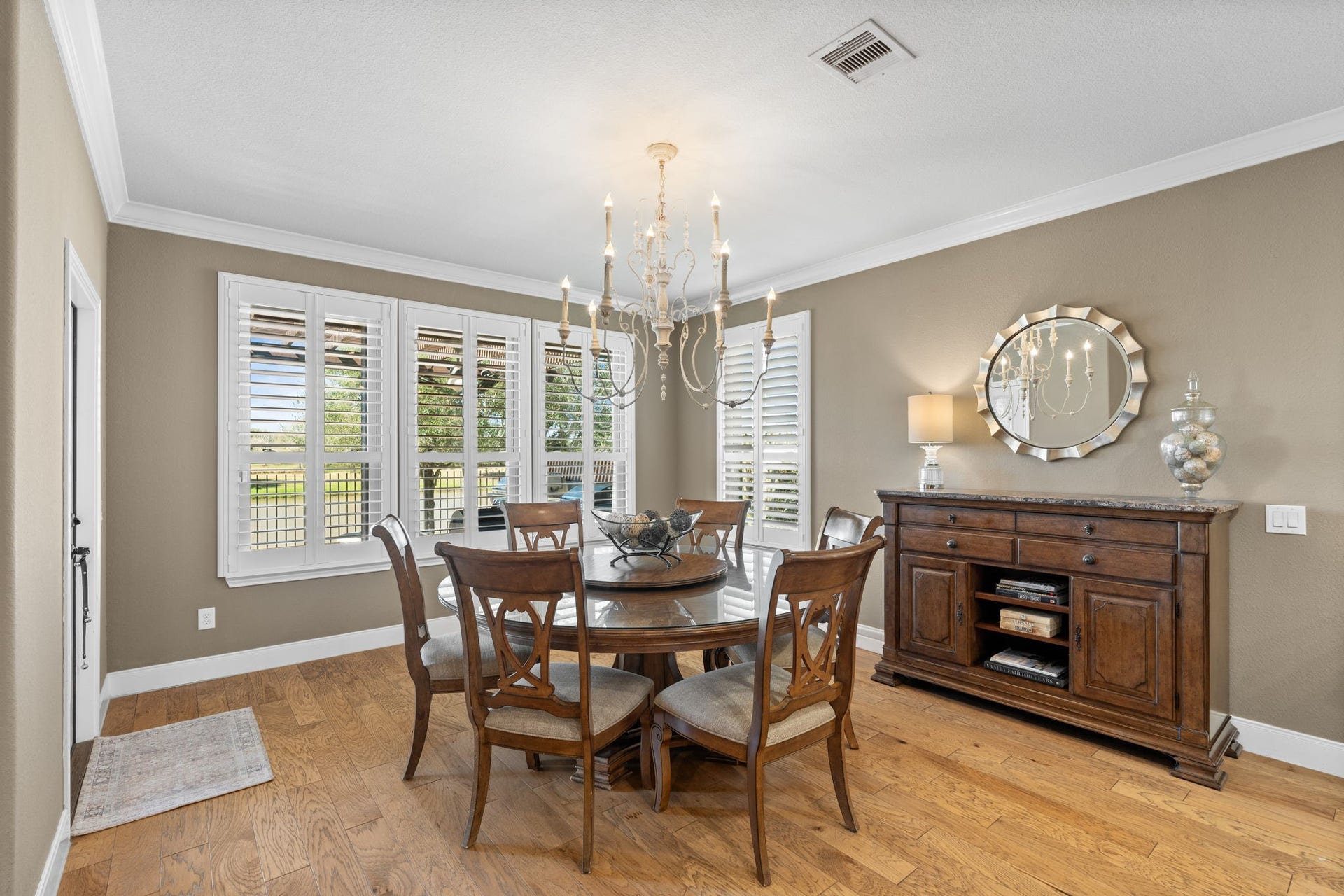 Spacious and elegantly appointed dining area with a modern hanging light fixture, hardwood floors, and neutral colors. White crown molding adds a classic touch, and the room flows seamlessly into adjacent living spaces