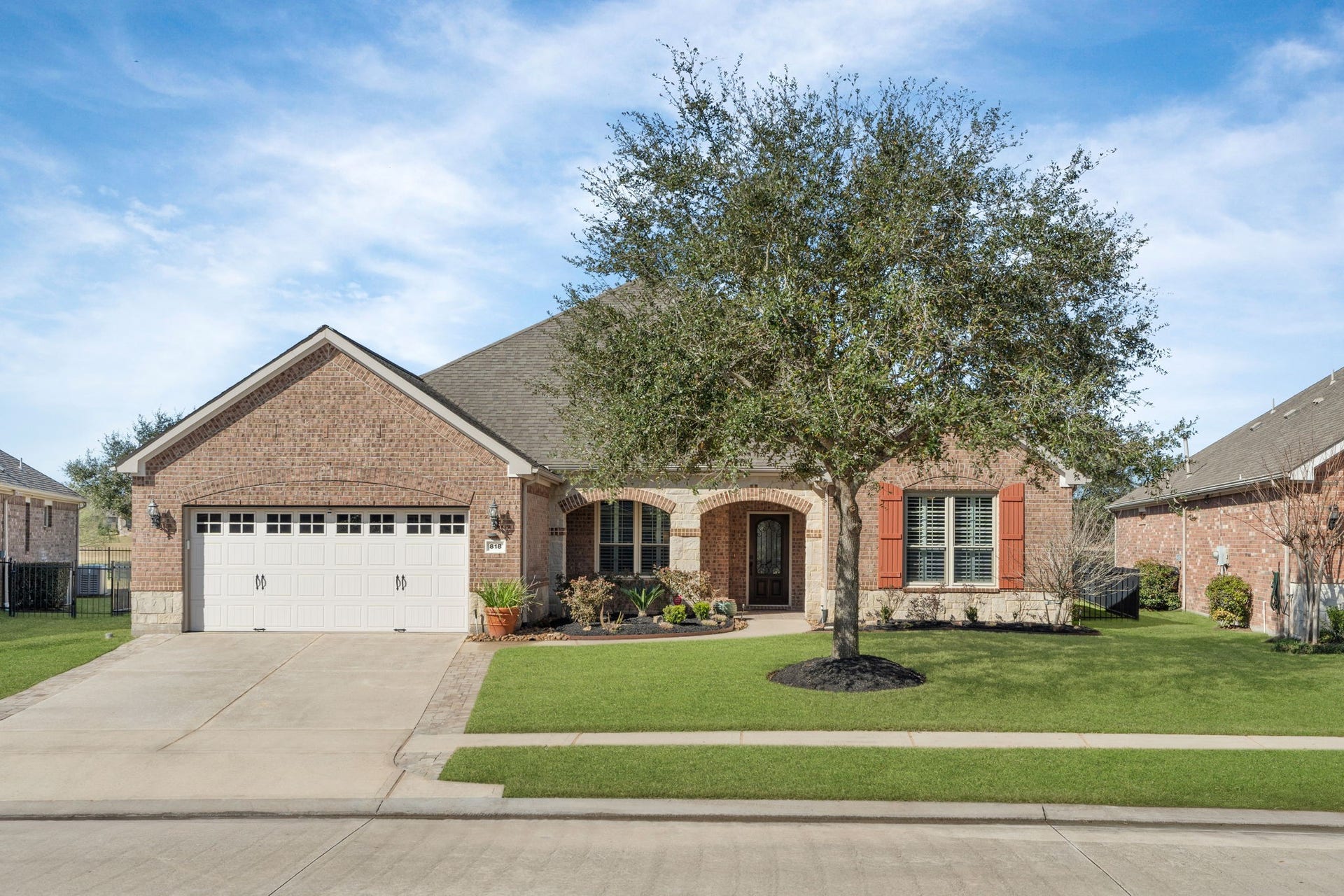 Charming architectural design featuring a blend of brick and stone, with two graceful arches framed by a stunning oak tree!