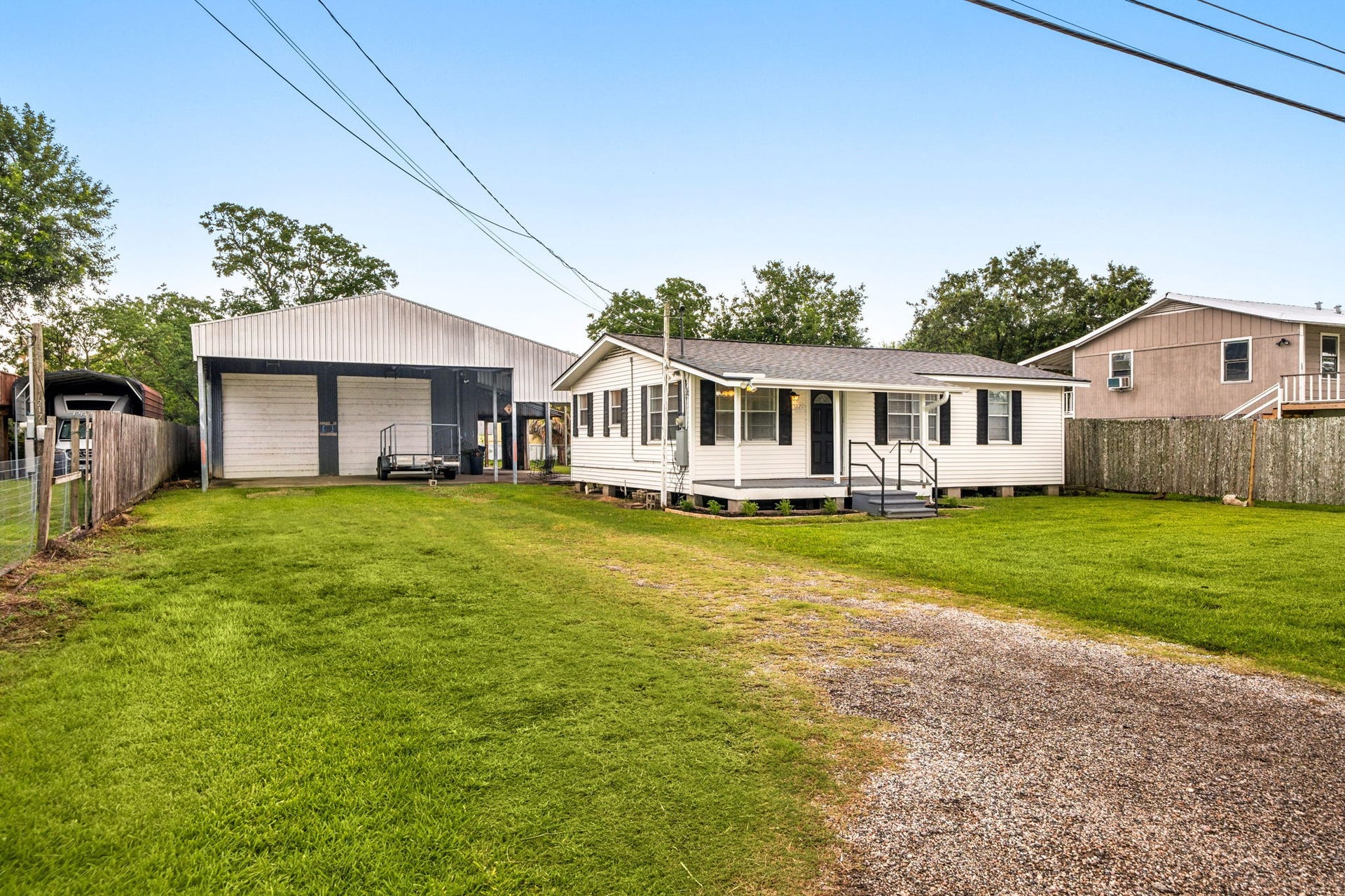 221 11th Street, San Leon, TX 77539 Charming single-story home with a welcoming front porch and spacious lawn. Features a large carport and a well-maintained fenced yard, perfect for family living. The house is set against a serene backdrop with mature trees, offering a peaceful neighborhood ambiance.