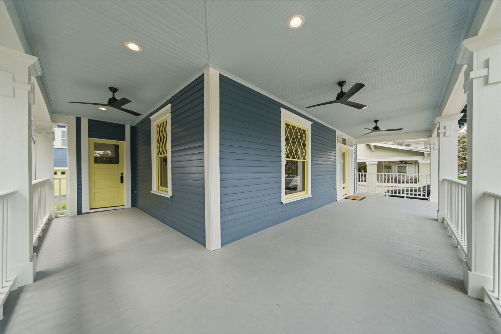 404 Avondale Street, Houston, TX 77006 Charming wraparound porch with elegant blue siding, accented by a cheerful yellow door and stylish ceiling fans, perfect for relaxing and entertaining.