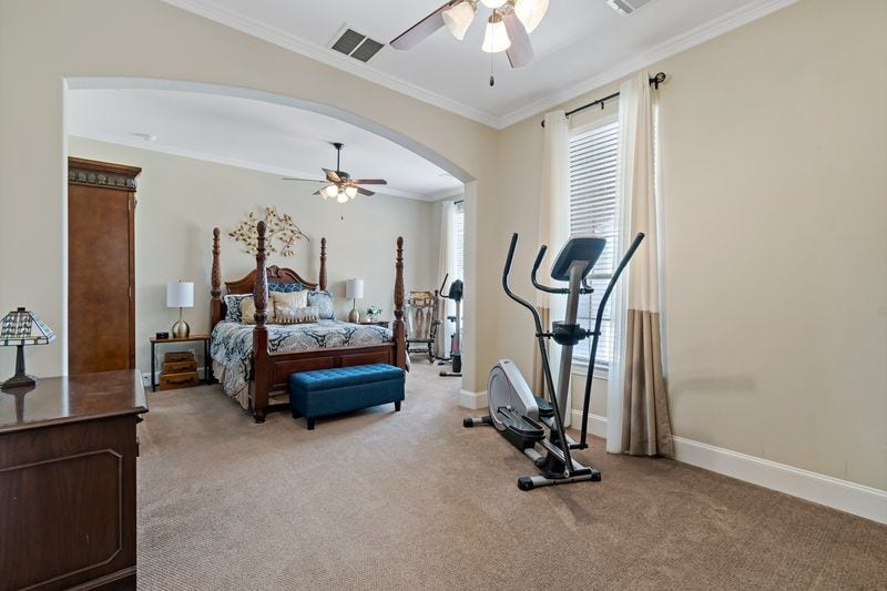 22 Waters Lake Boulevard, Missouri City, TX 77459 Spacious master bedroom with elegant four-poster bed, cozy carpeting, and an adjoining exercise area, flooded with natural light from large windows.