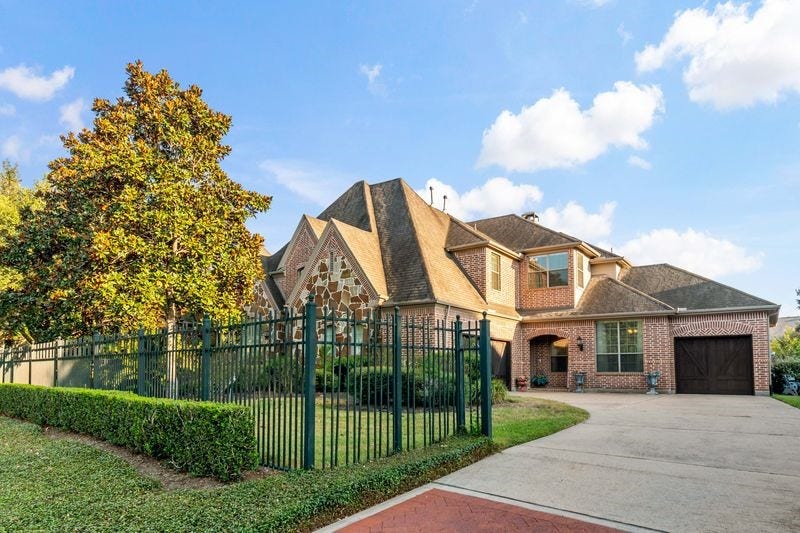22 Waters Lake Boulevard, Missouri City, TX 77459 Stunning brick home with a charming gabled roof, spacious driveway, and a beautifully landscaped front yard, all enclosed by an elegant wrought-iron fence.