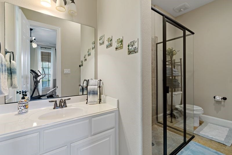 22 Waters Lake Boulevard, Missouri City, TX 77459 Modern bathroom featuring a sleek glass shower enclosure, elegant white vanity, and well-placed lighting, adjacent to a bright exercise area.